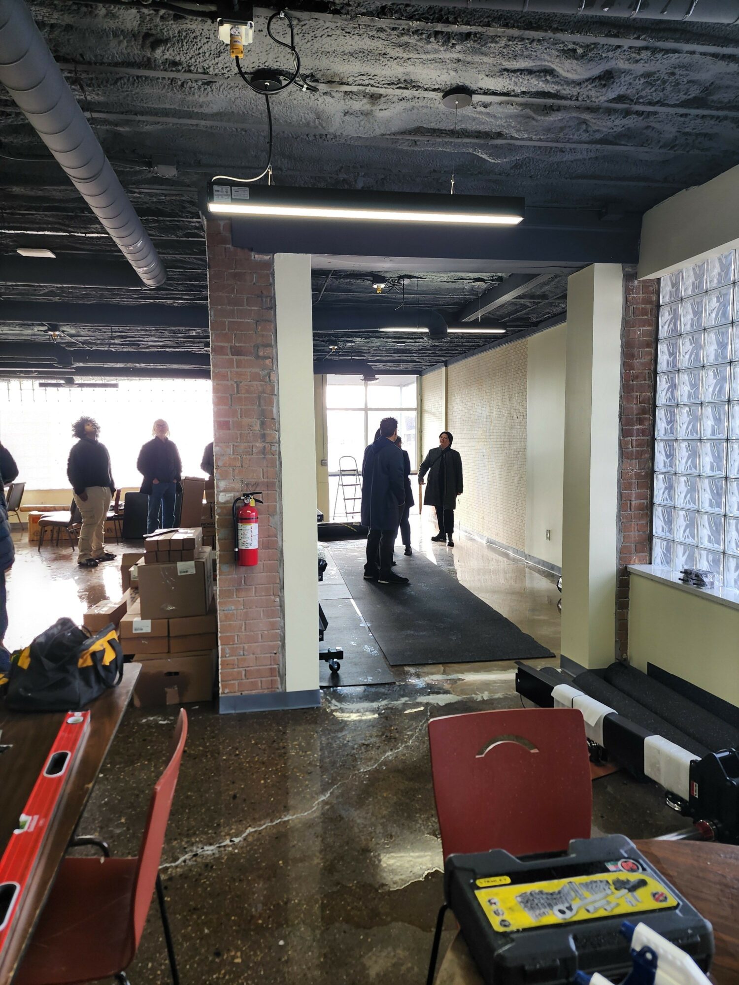 People walking in a modern indoor space with brick columns and large windows, viewed from a tilted angle.