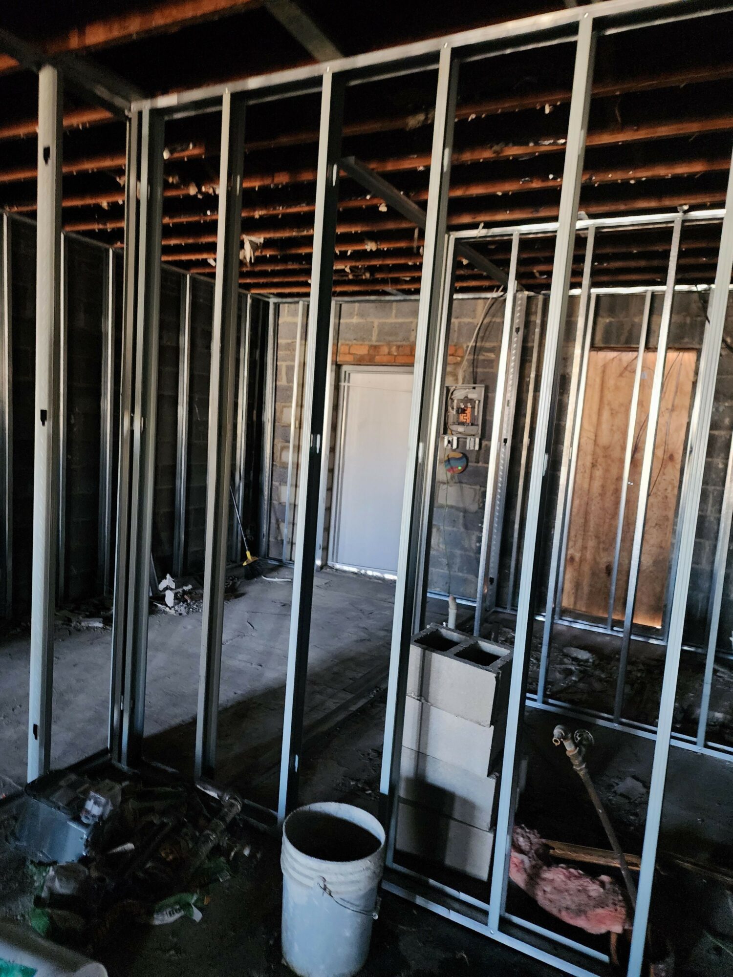 View through metal bars of an indoor construction site with wooden and metal structures, a white bucket, and construction materials.