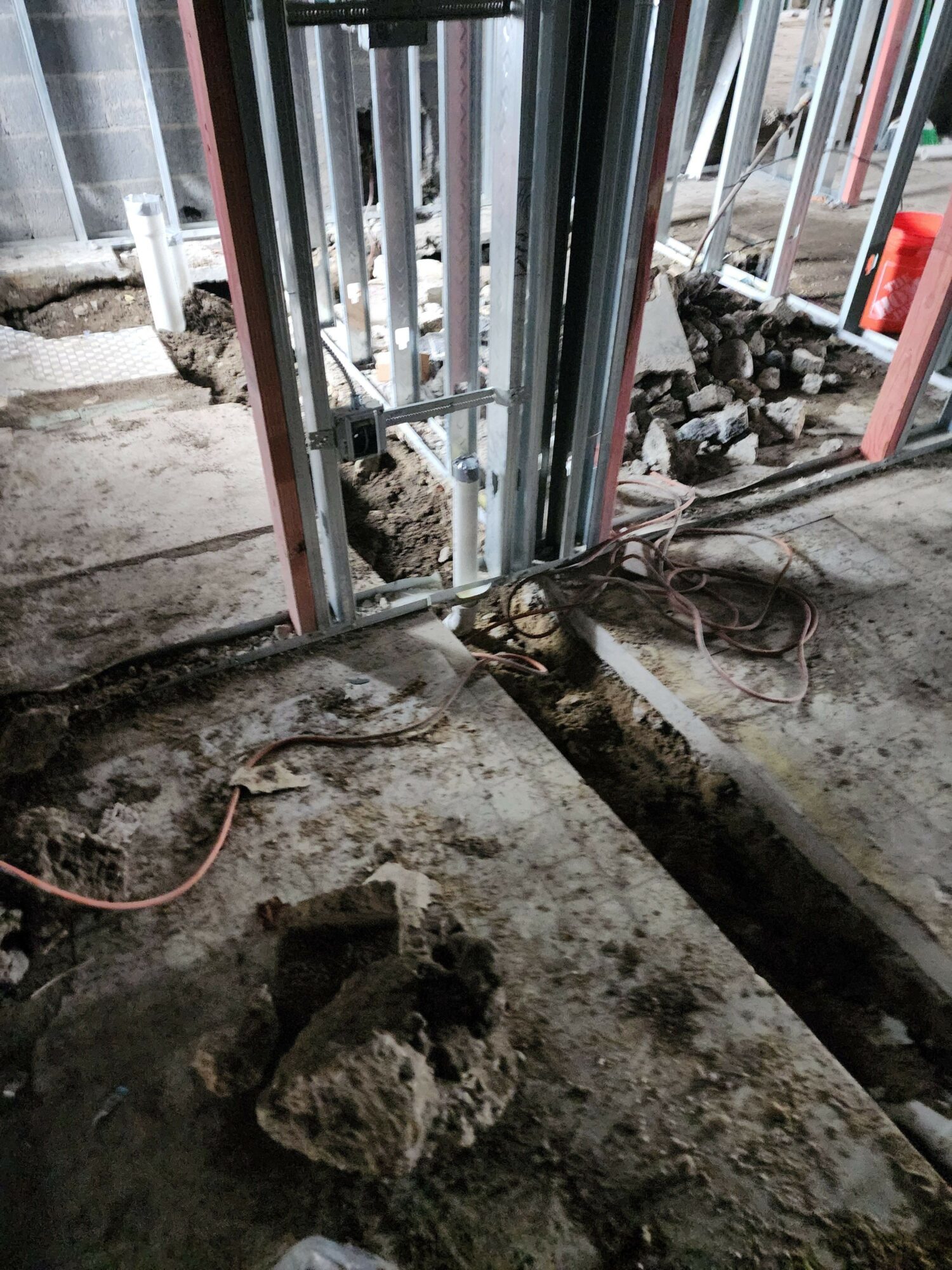 Construction site with metal pipes, rocks, and cables on a concrete floor, viewed from the side.