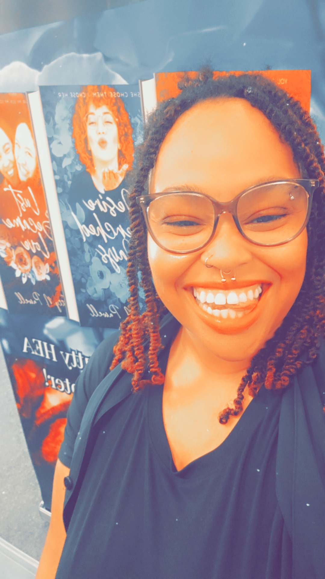 Smiling woman with glasses and curly hair taking a selfie in front of colorful posters.