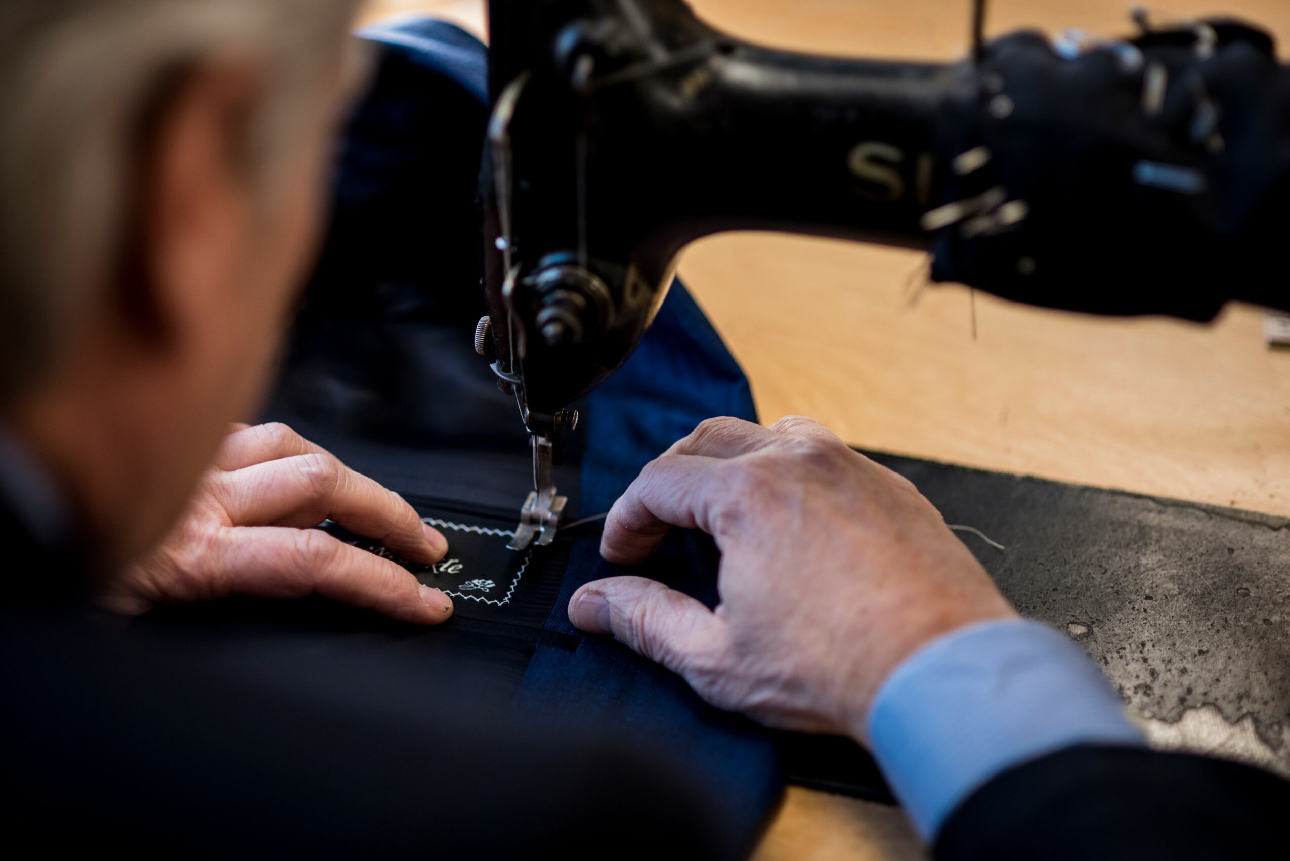 Person sewing fabric with a sewing machine, hands guiding material, blurred background, close-up view.