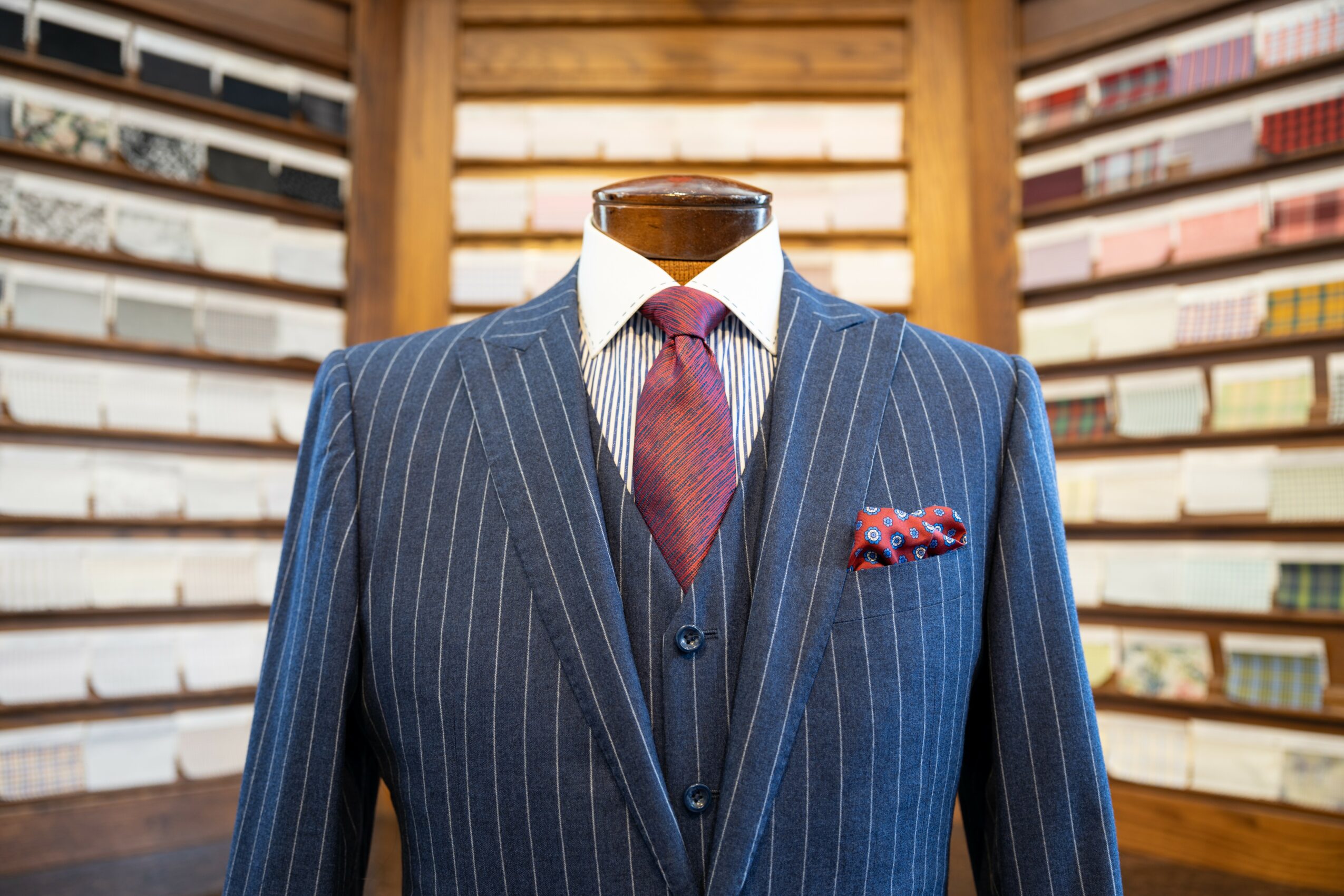 Mannequin dressed in a pinstripe suit with a tie and pocket square, in front of a bookshelf background.