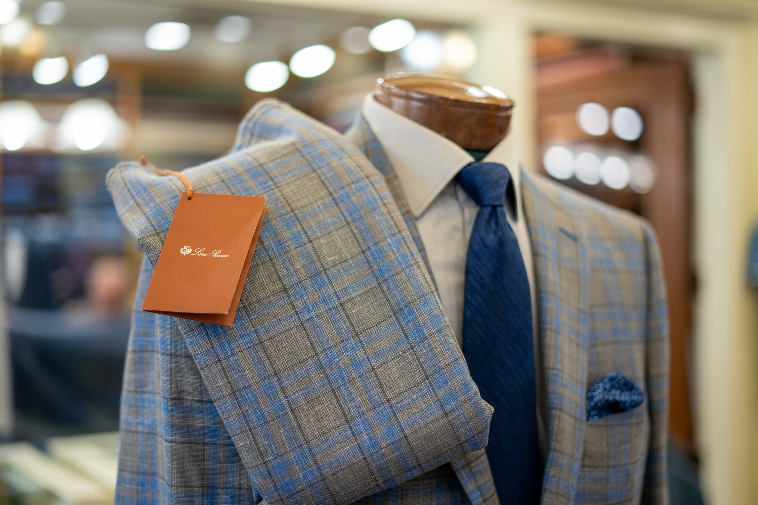 Mannequin dressed in a plaid suit with a white shirt and blue tie, with a matching plaid blazer draped over shoulder, in a store display.