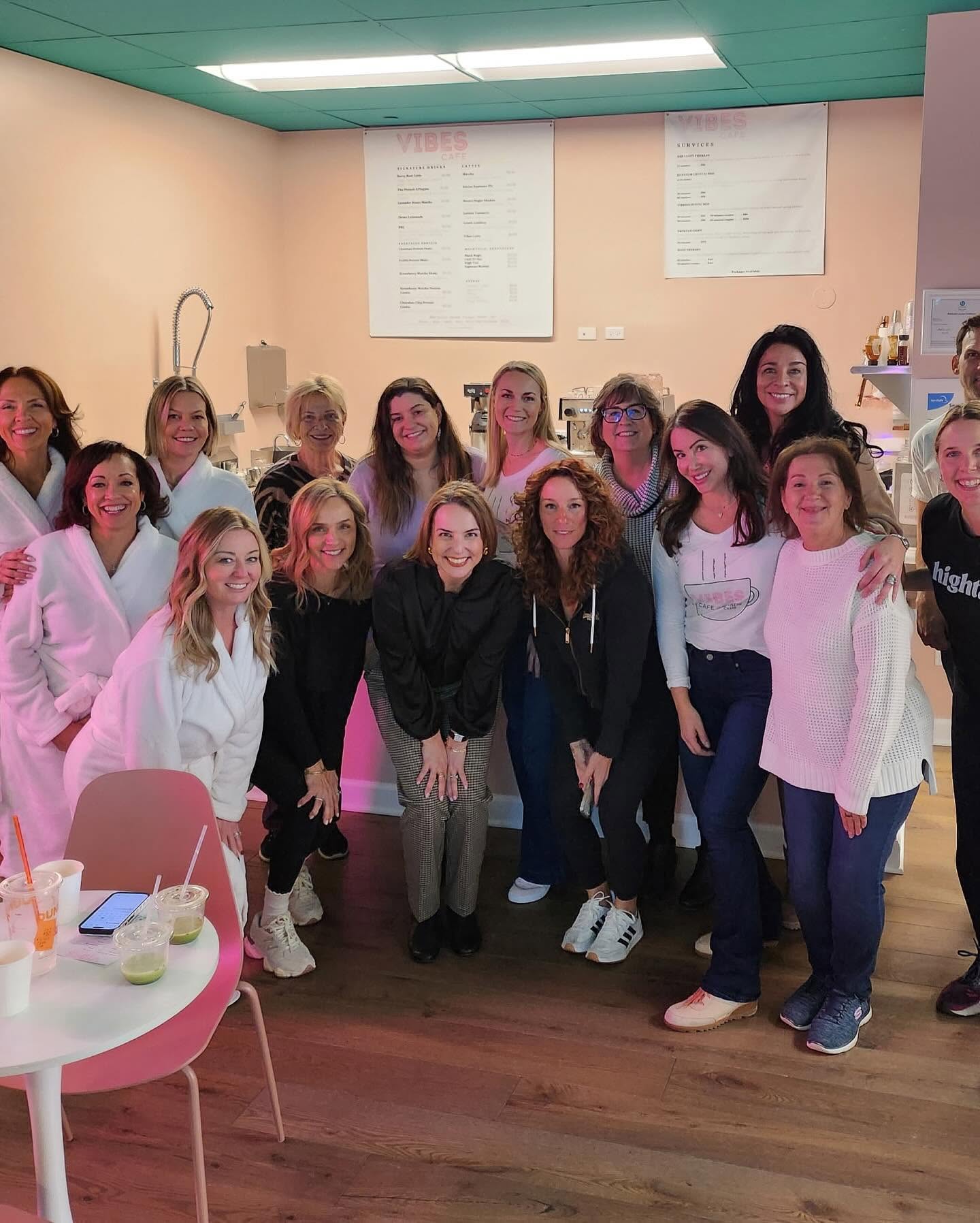Group of women standing together indoors, smiling, with a menu board on the wall behind them.
