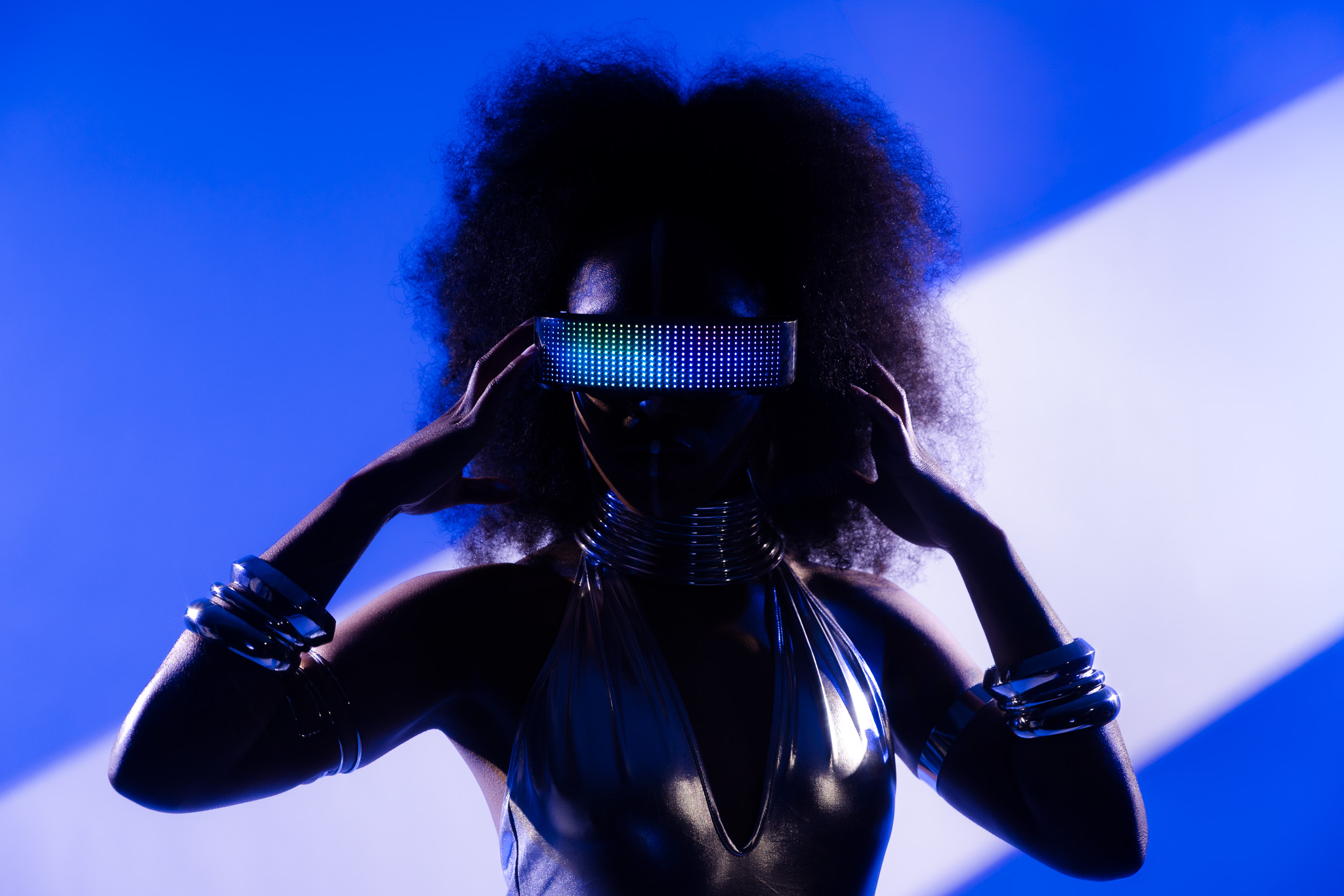 Silhouette of a person with curly hair, wearing reflective accessories, against a blue background.