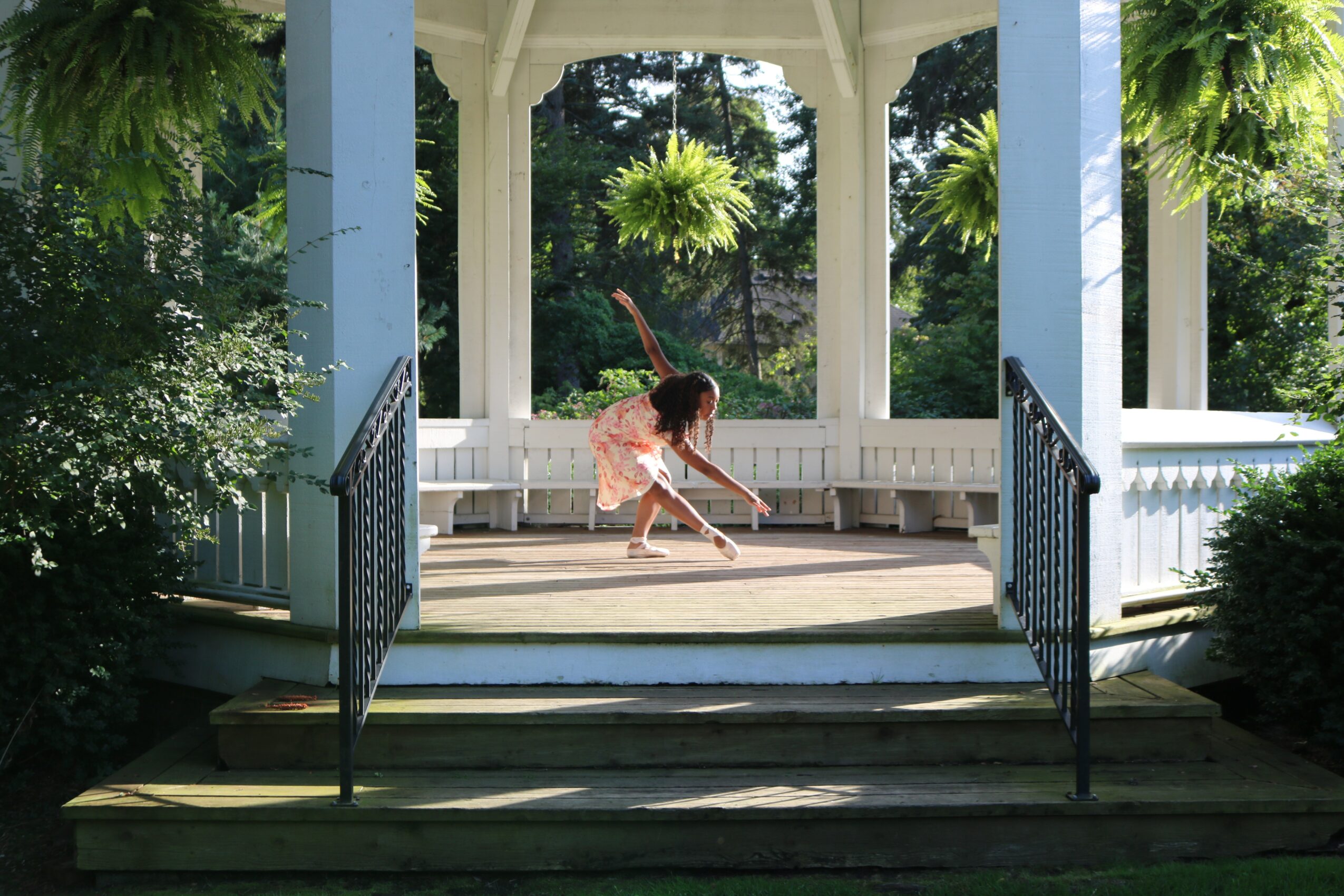 Person sweeping the floor of a gazebo with white columns, surrounded by greenery and trees.