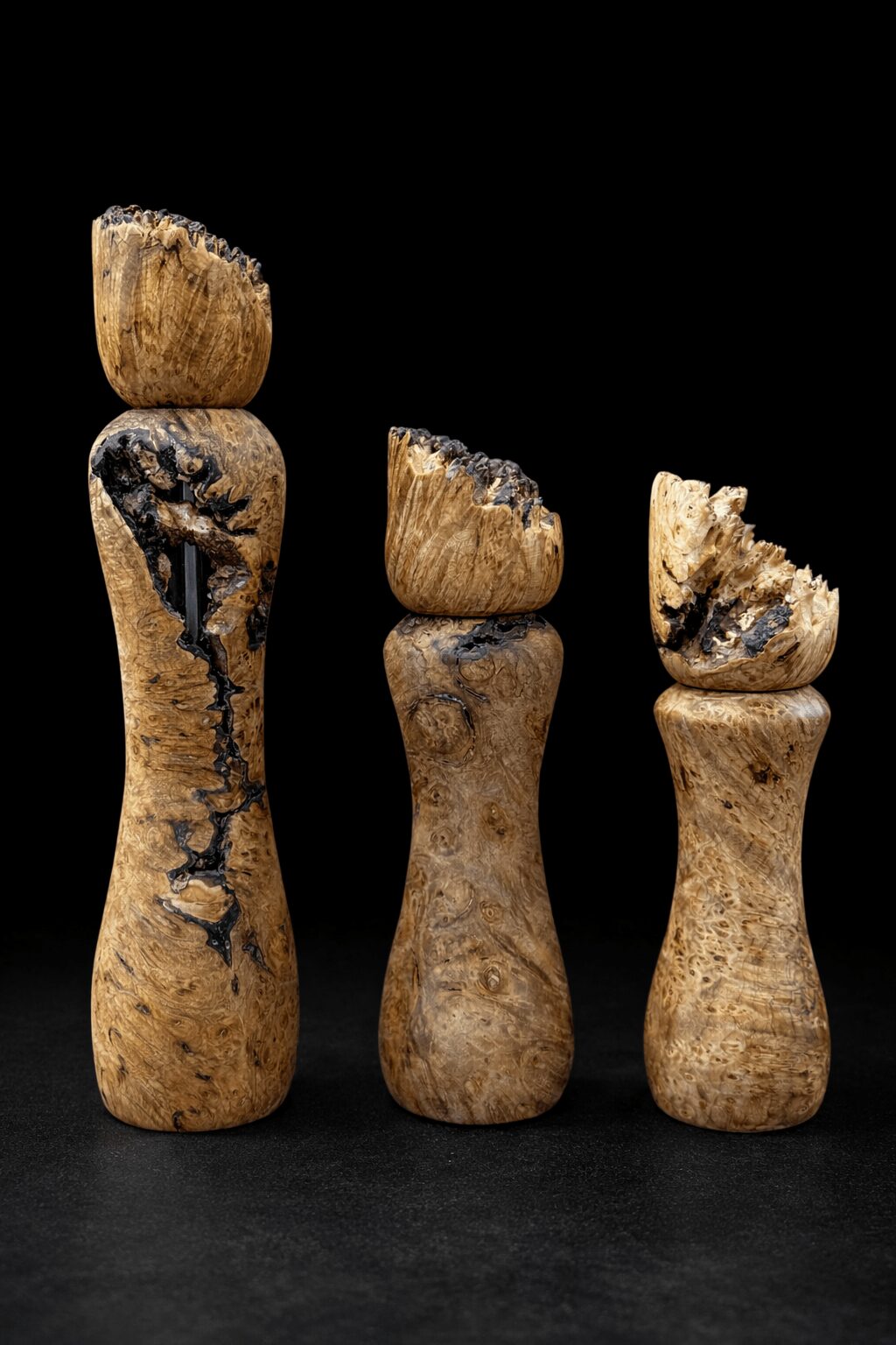 Three wooden objects with broken tops, varying in height, against a black background.