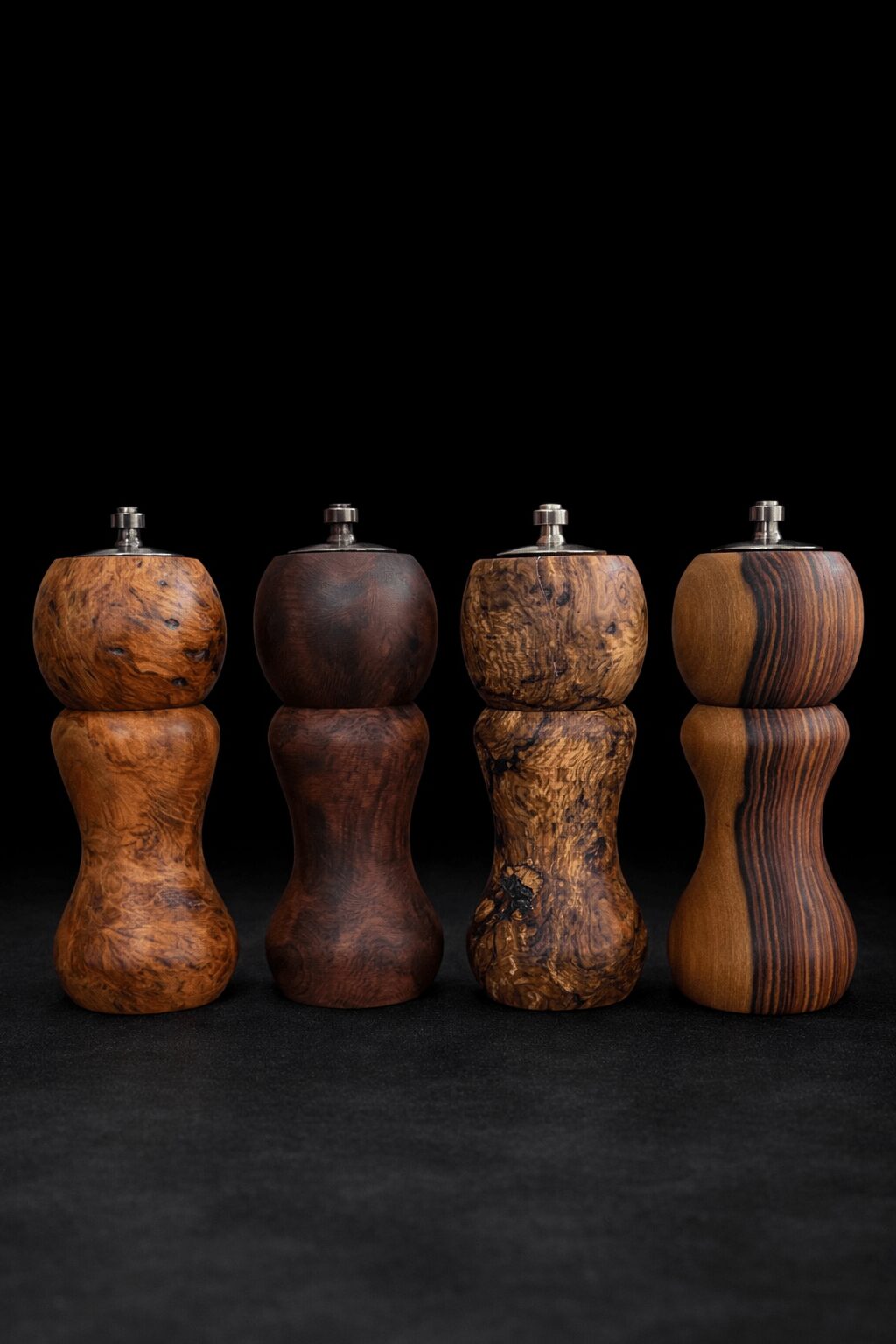 Four wooden salt and pepper shakers with different shapes and wood grains, set against a black background.