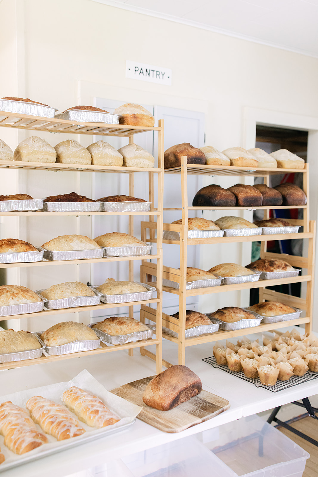 Two wooden shelves filled with various types of bread in a bakery, with a sign labeled 'PANTRY' above.