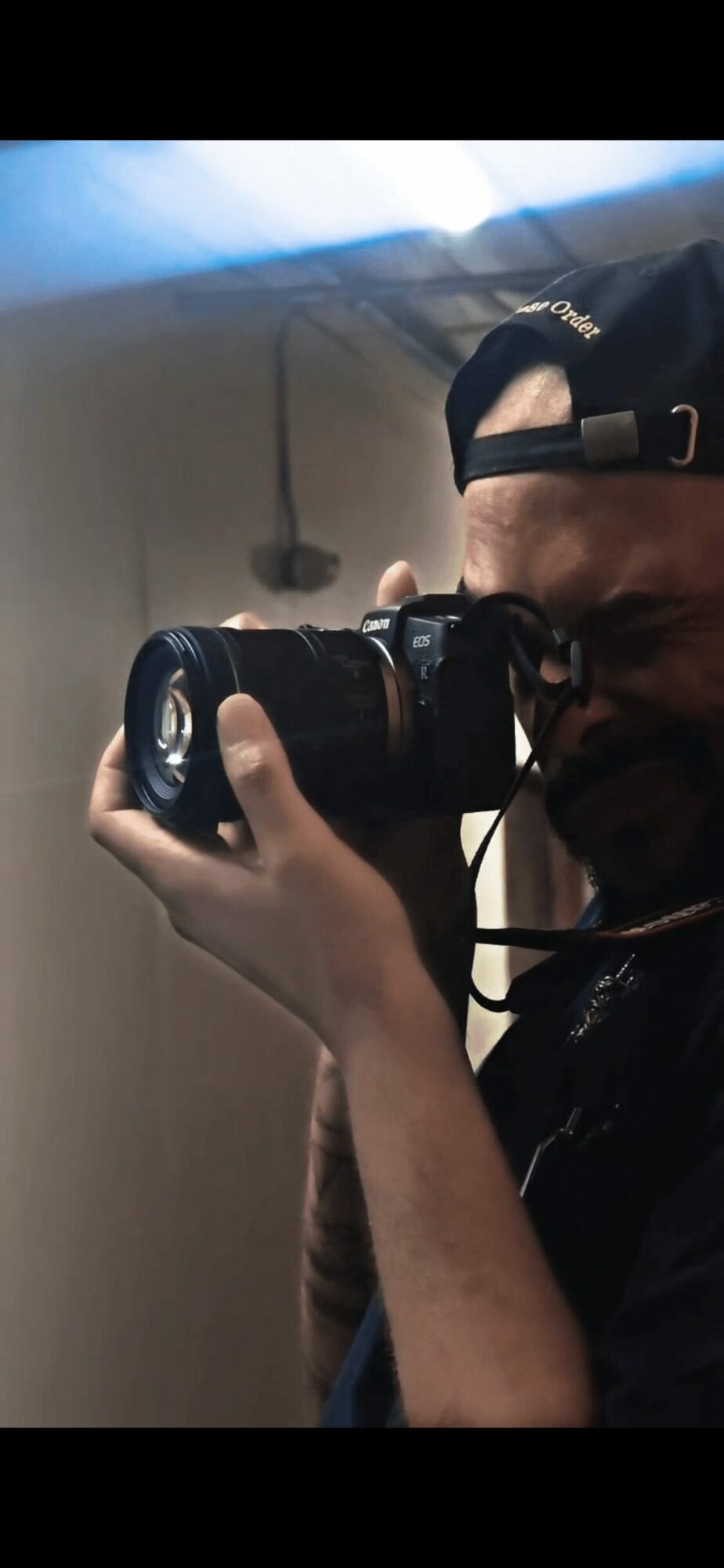 Person taking a photo with a camera, wearing a cap backwards, in a room with a ceiling fan.