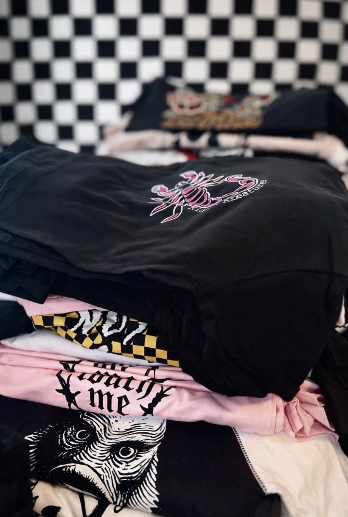Stacked clothes on bed with black and white checkered wall in background.