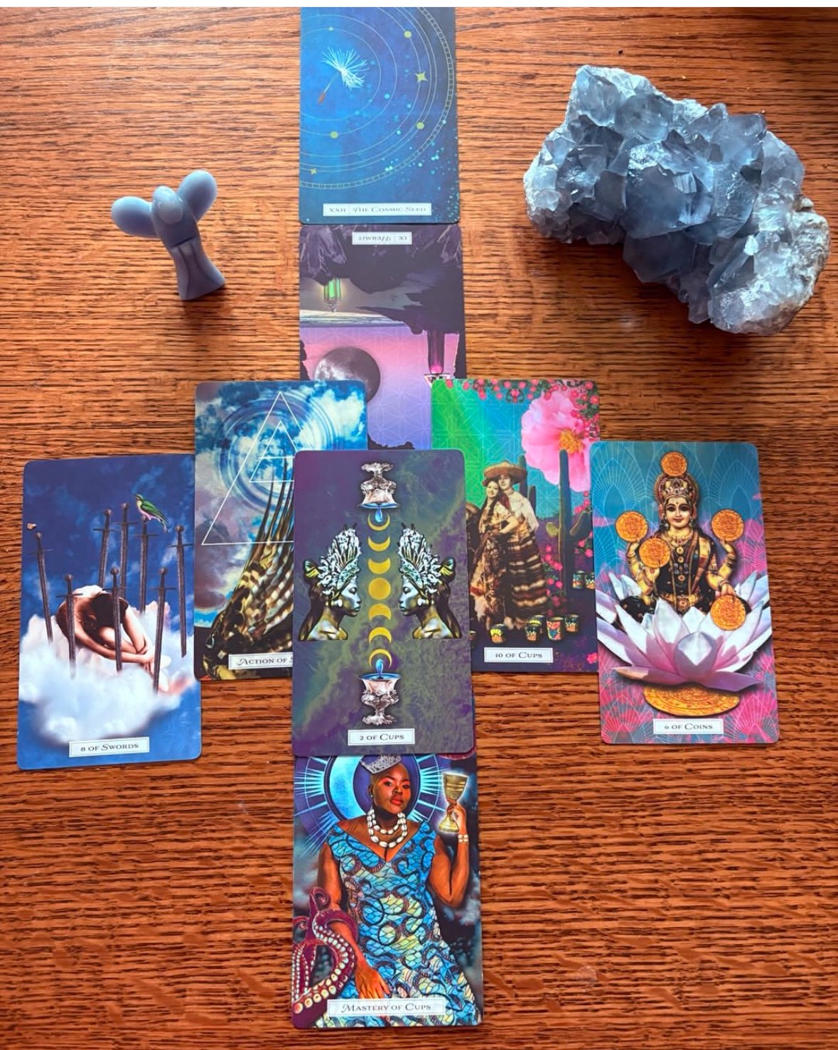 Six tarot cards, a blue crystal, a small cactus-shaped object, and a vertical card on a wooden surface.