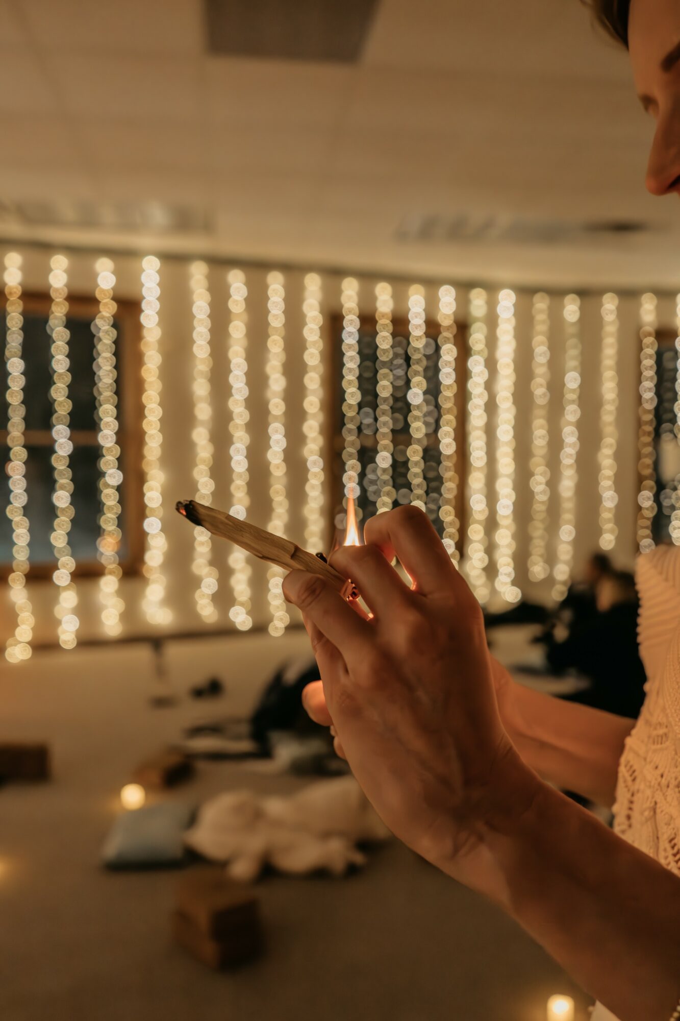 Person holding a smartphone with a background of hanging string lights, indoor setting, warm lighting.