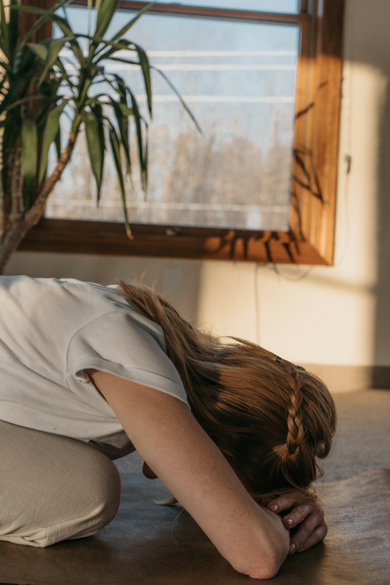 Person lying on the floor with head resting on hands near a window with sunlight and shadows.