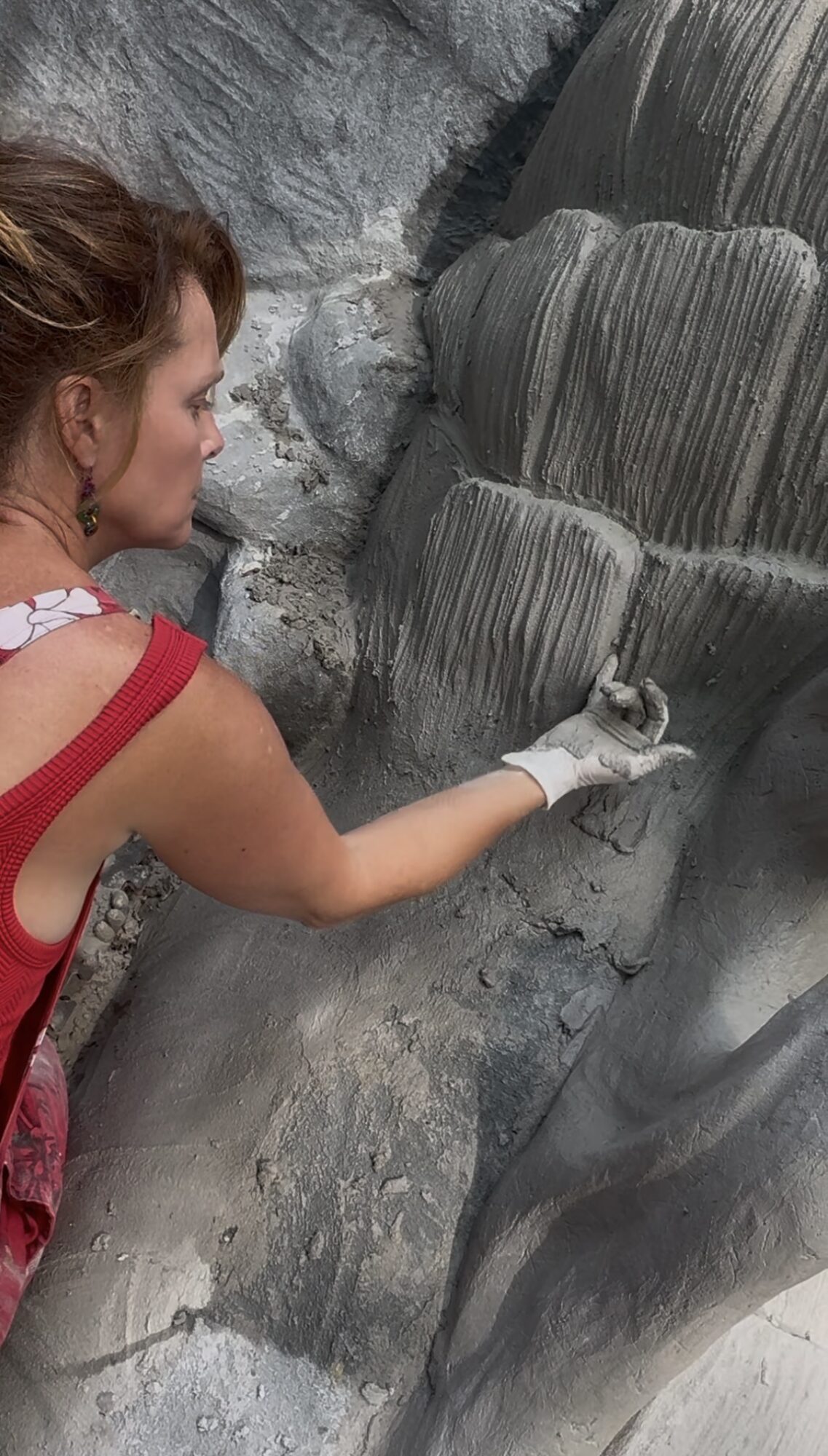 Woman painting a large, textured sculpture with a brush, wearing a red top and white glove.