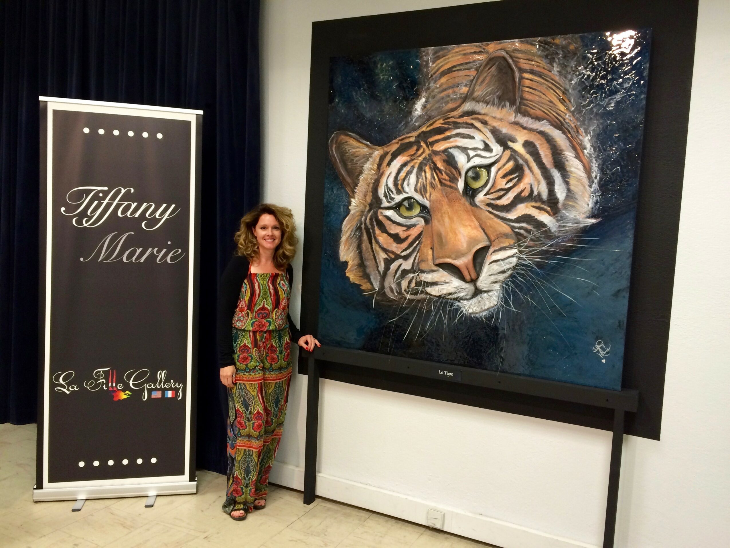 Woman standing next to a large tiger painting at an art gallery, with a sign reading Tiffany Marie nearby.