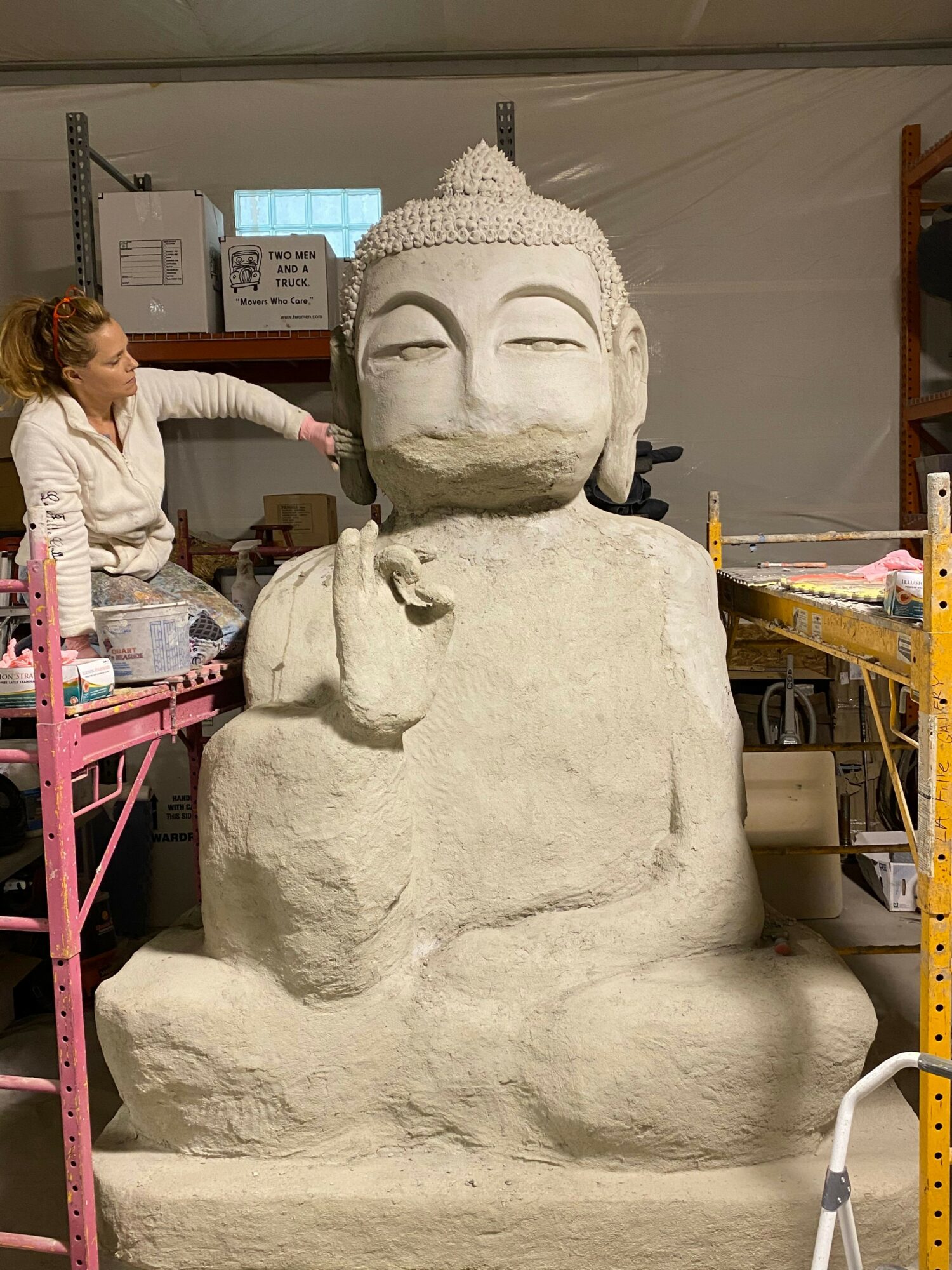 Large stone sculpture of a person with a hat, resting on a workbench in a workshop.
