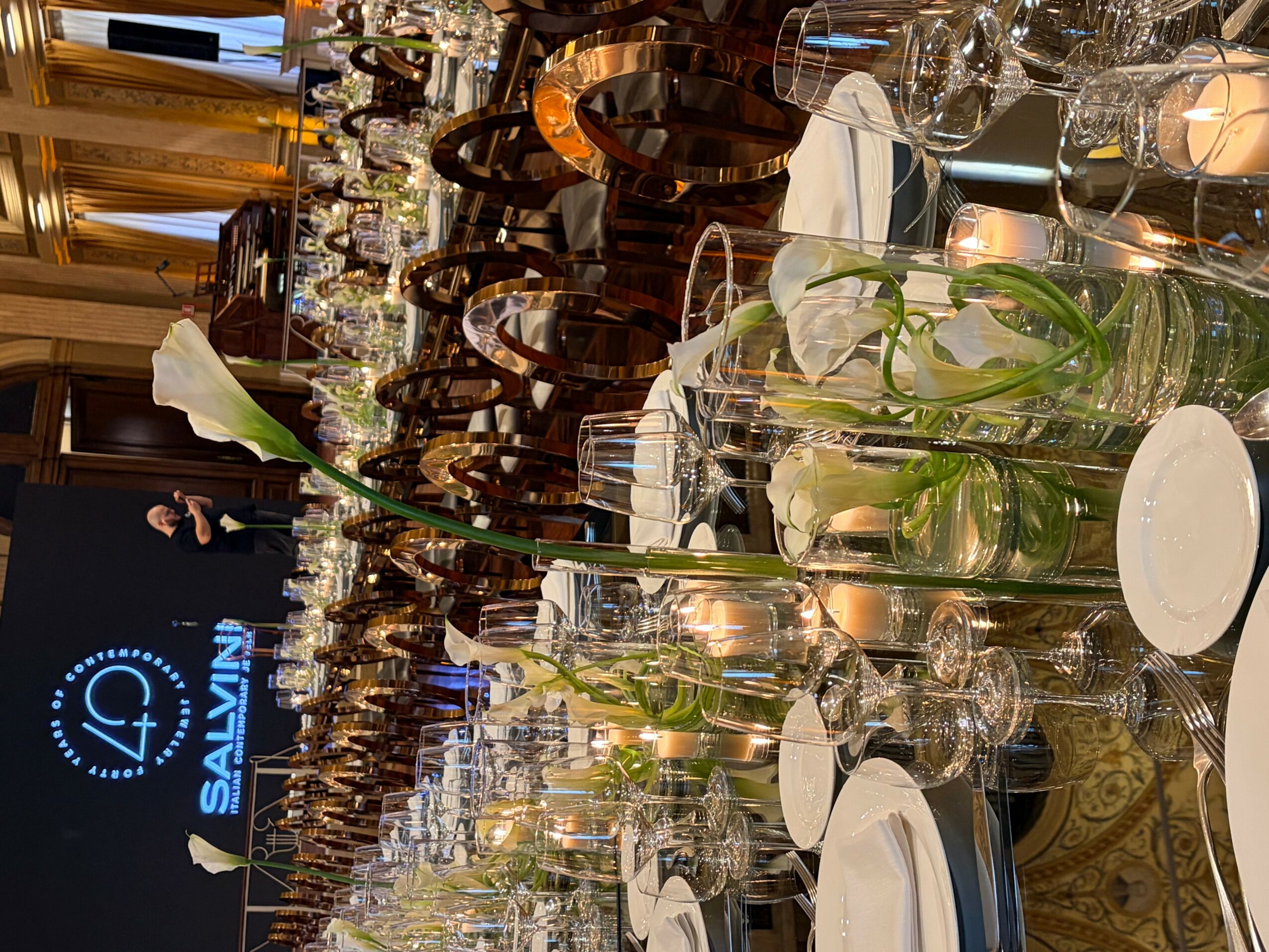 Elegant dining table with white flowers in glass vases, set with plates, glasses, and silverware, in a luxurious room.