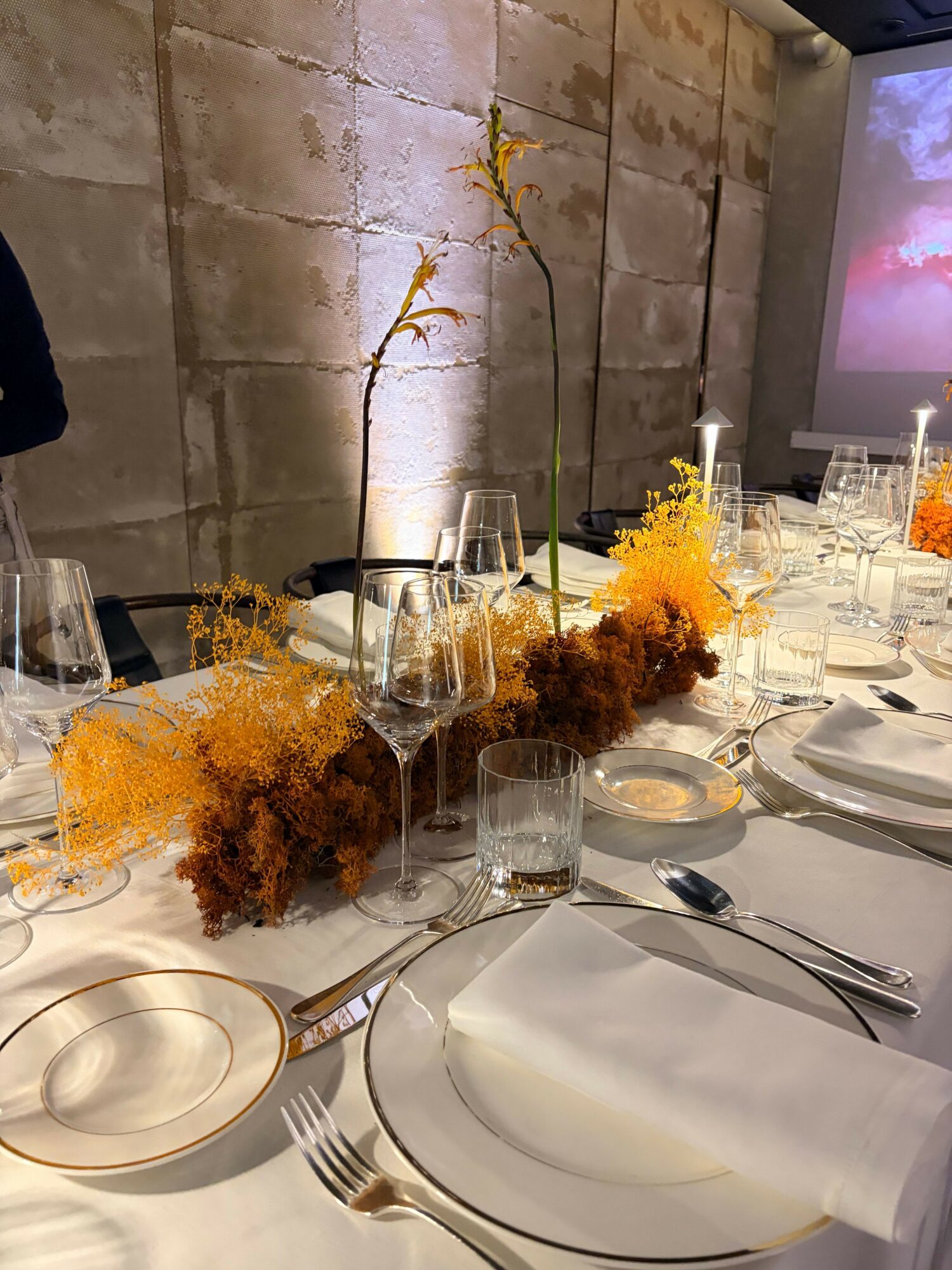 Table setting with plates, glasses, and floral centerpieces on a white tablecloth.