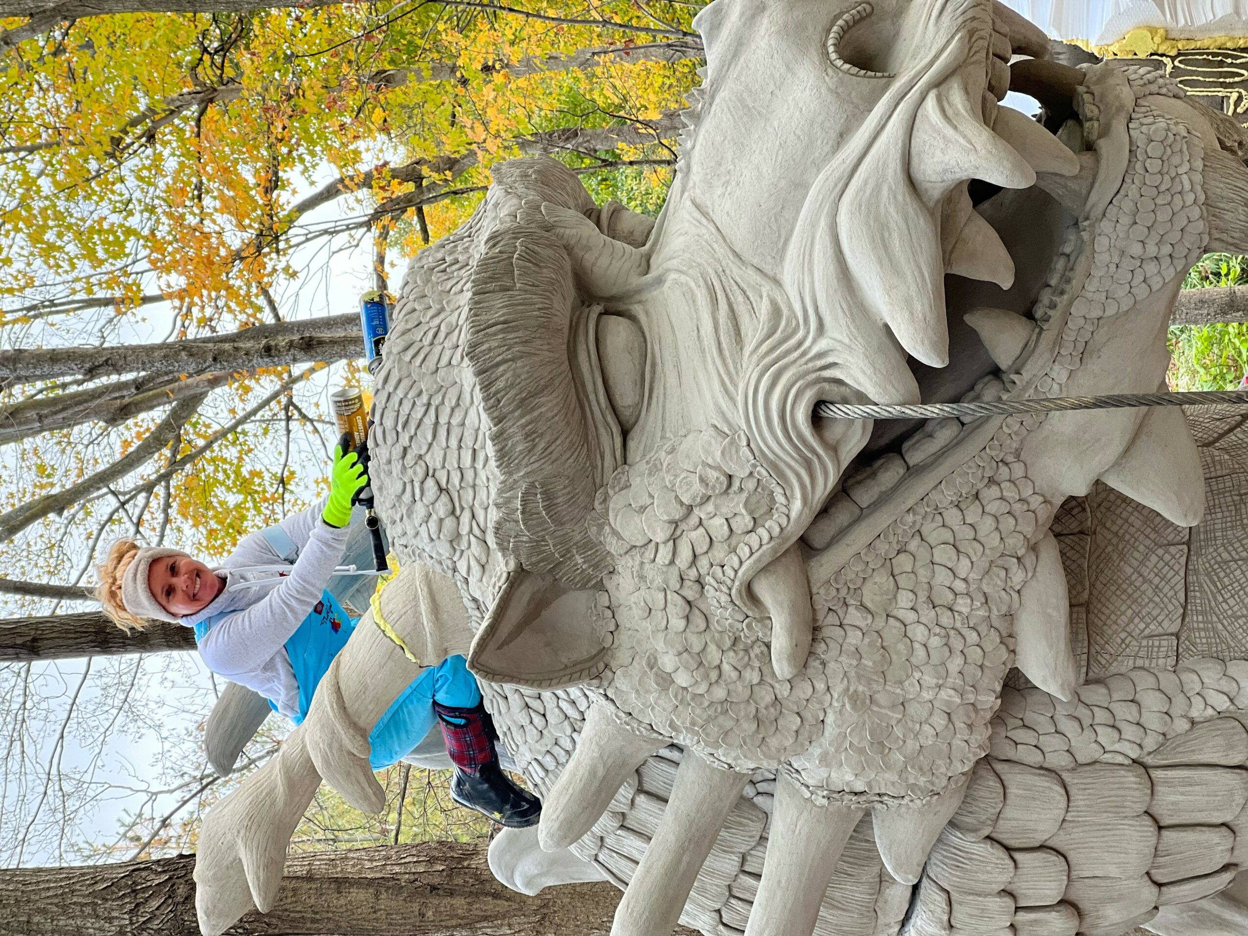 Child climbing a large stone dragon sculpture outdoors with trees and autumn leaves in background.
