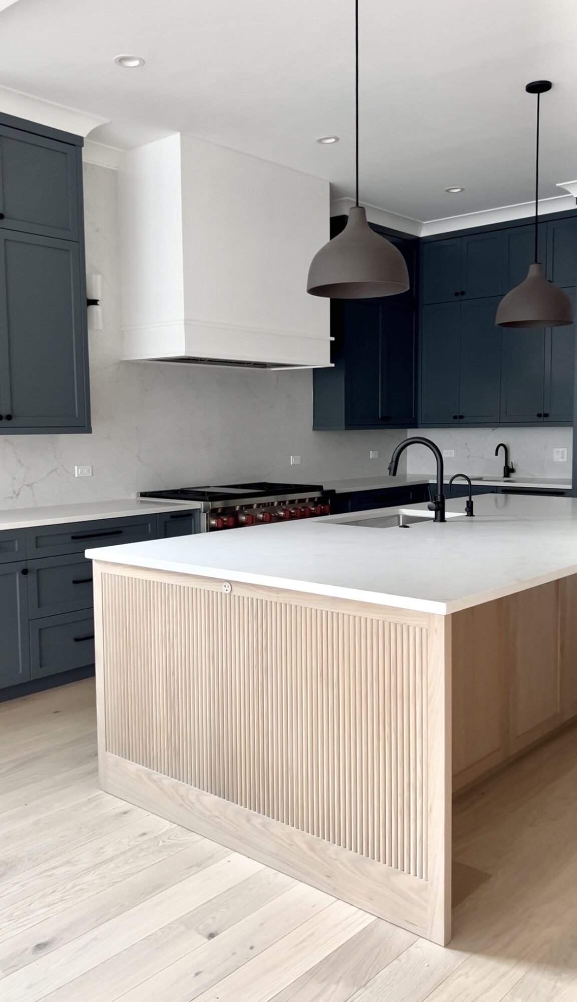 Modern kitchen with dark blue cabinets, white countertops, and a light wood island, pendant lights hanging from ceiling.