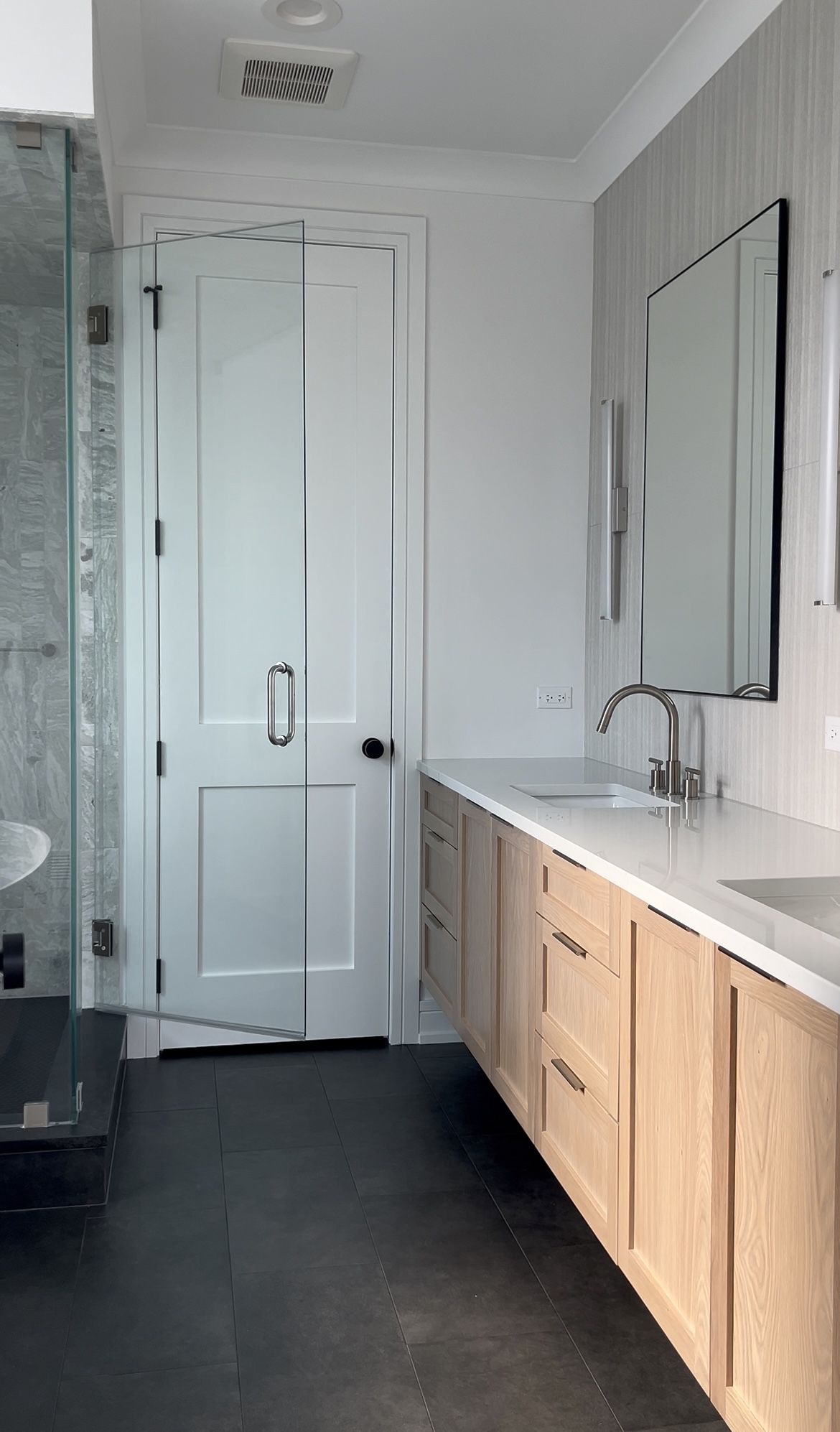 Bathroom with wooden vanity, mirror, faucet, glass shower door, and white walls.