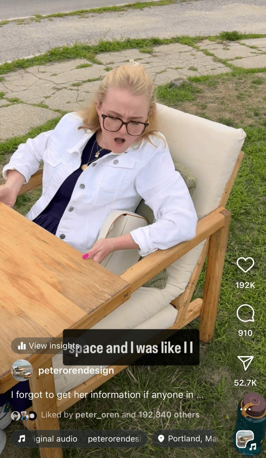 Young girl with glasses sitting in a chair outdoors, mouth open, wearing a white shirt and dark top, next to a wooden table.