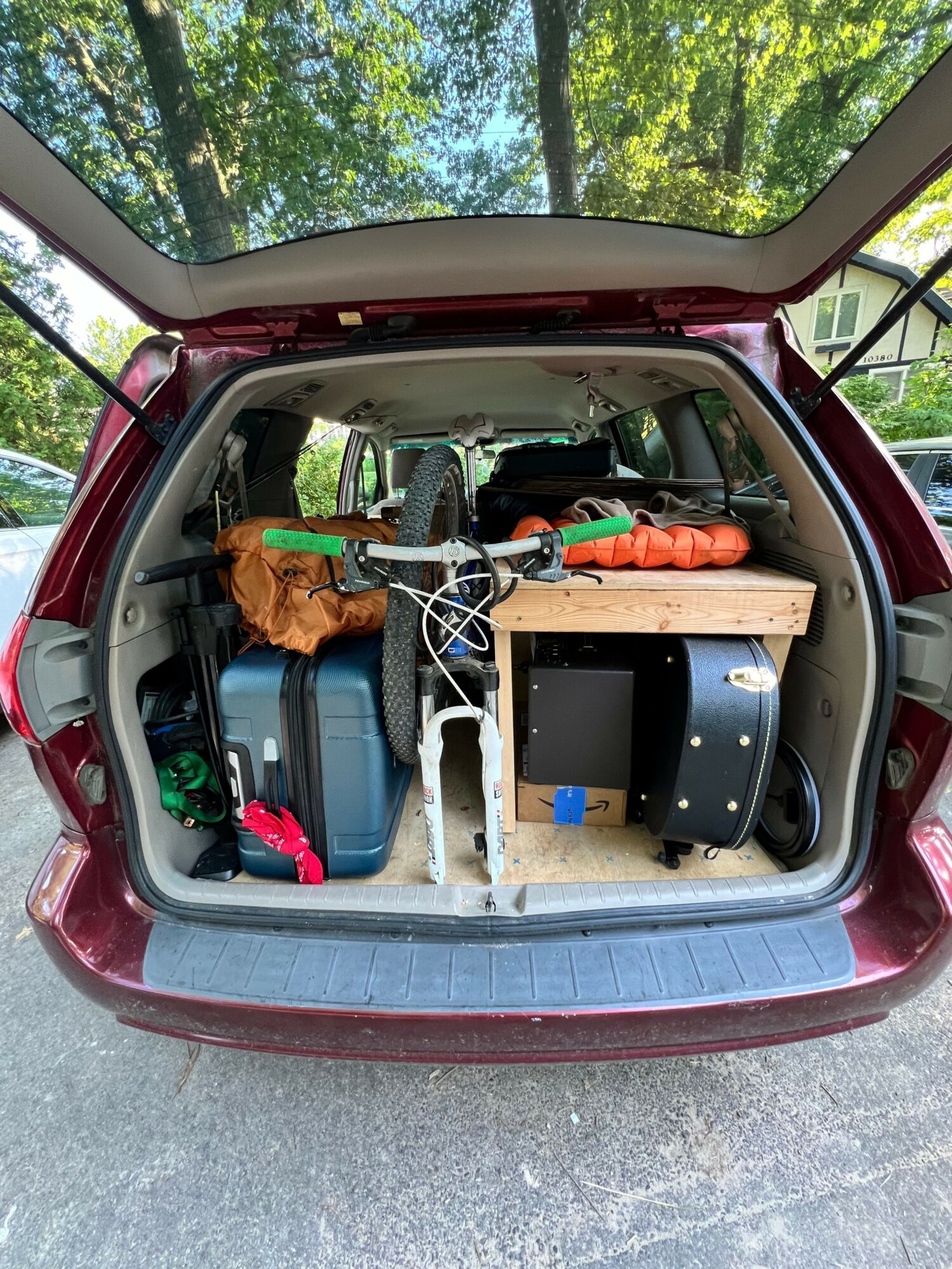 Open trunk of a red vehicle filled with camping gear and supplies, including a cooler, bags, and a wooden crate.