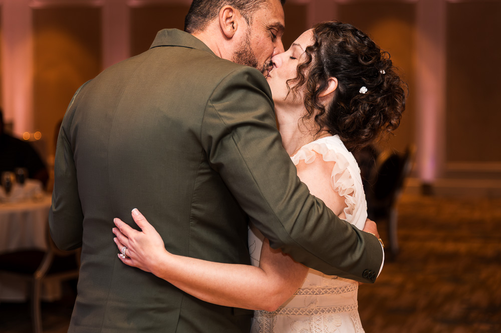 A couple dancing closely at a formal event, with warm lighting and blurred background, embracing each other.