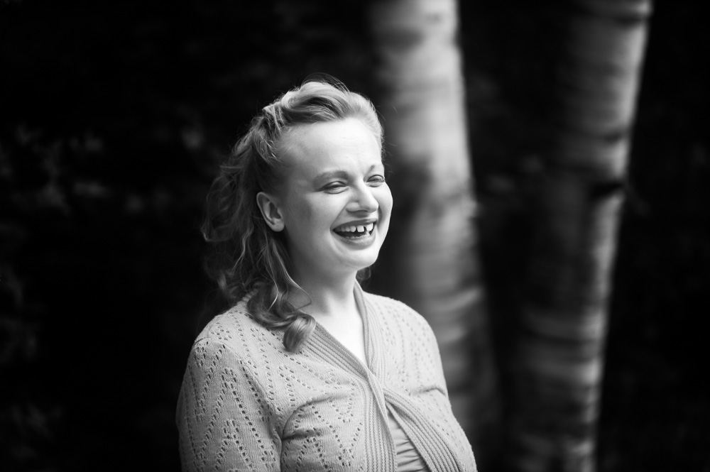 Smiling woman with wavy hair outdoors, trees in background.