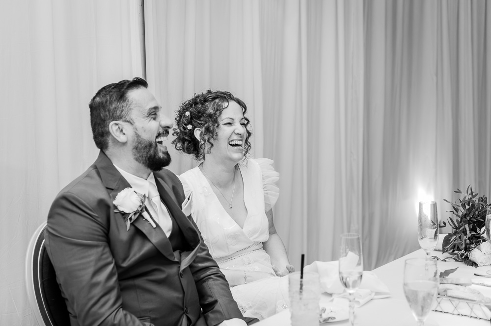 Two people laughing at a table during a celebration, with curtains in the background.