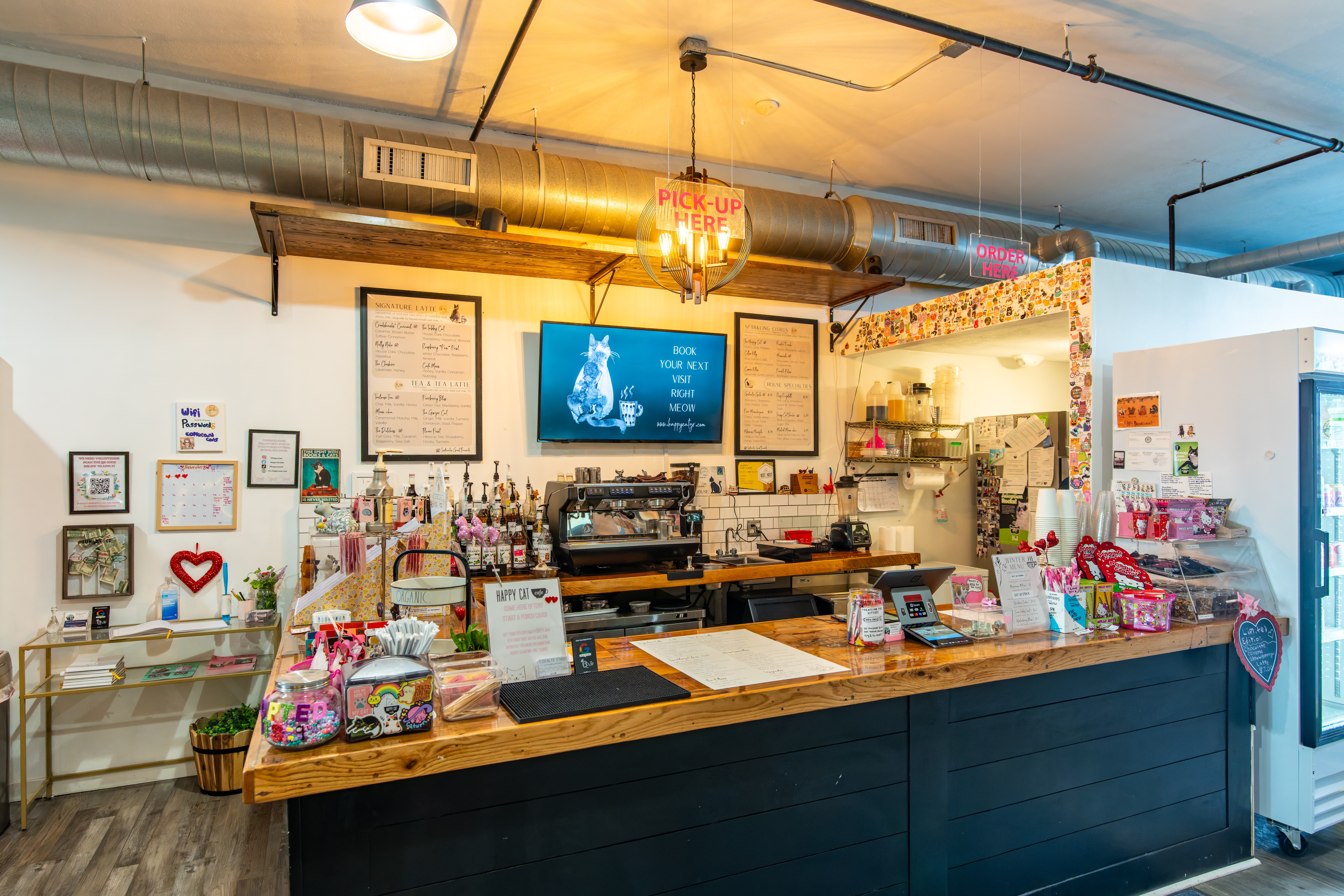 Counter with various items, shelves, framed pictures, and a TV screen in a cozy shop interior.