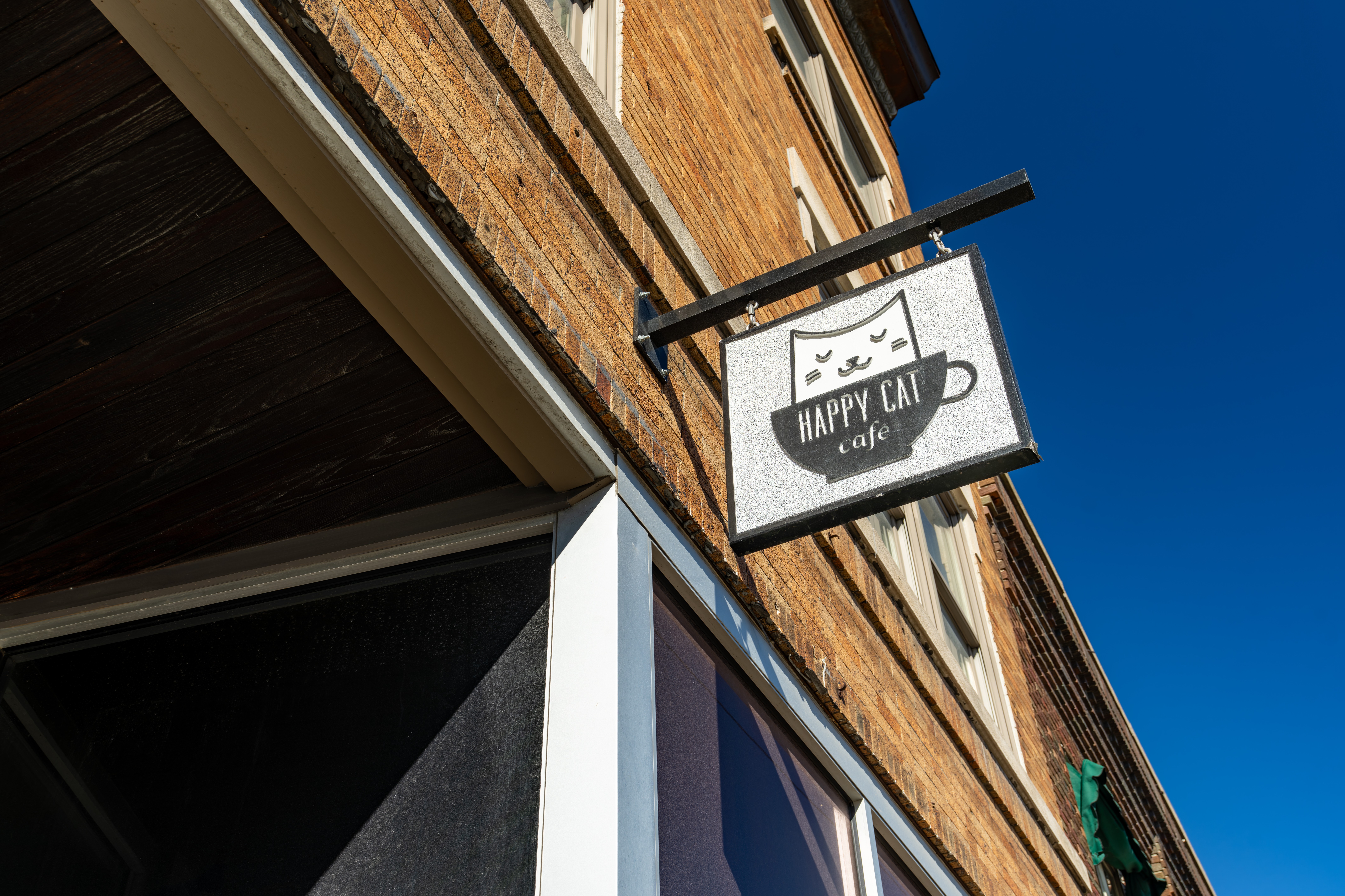 Signboard with a coffee cup and the text 'HAPPY CAFE' hanging outside a brick building against a blue sky.