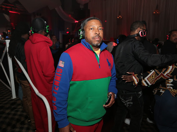 Man wearing headphones and a colorful jacket in a crowded indoor event with dim lighting.
