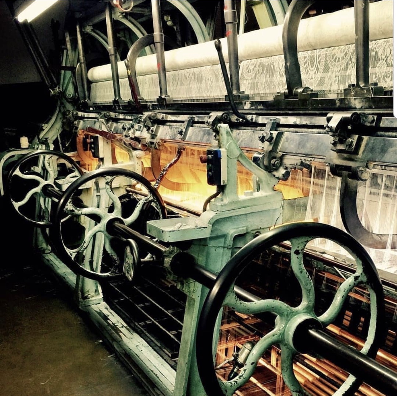 Industrial machinery with large wheels and levers, illuminated by orange and white lights, in a factory setting.