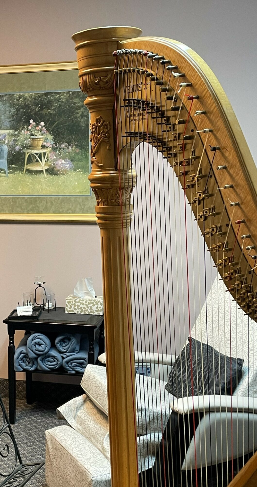 Upright harp with a wooden column and strings, in a room with a window and furniture.
