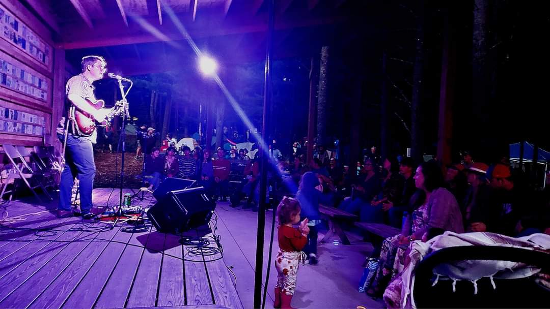 Musician performing on stage with audience watching in a dimly lit venue.
