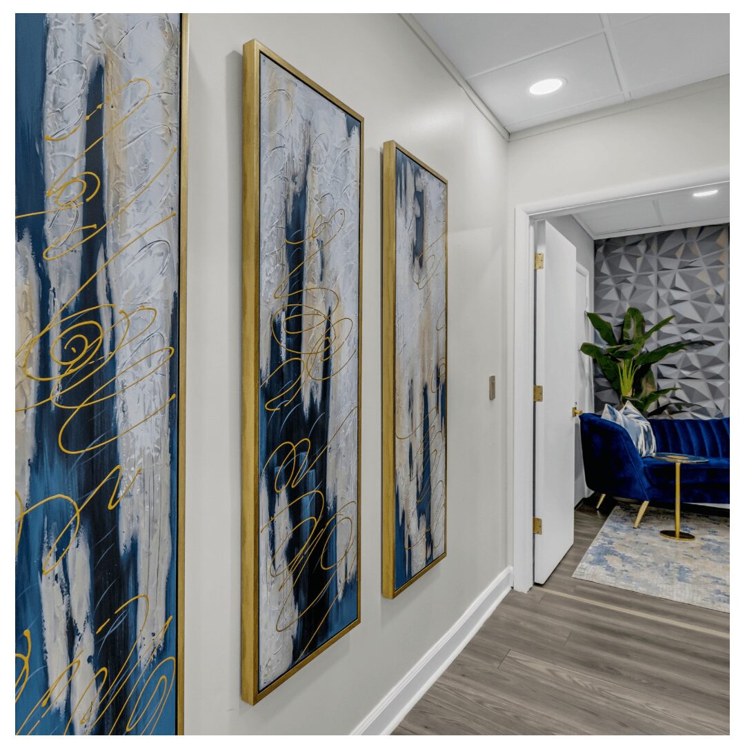 Three vertical abstract paintings with blue, white, and gold accents hang on a white wall in a modern interior.