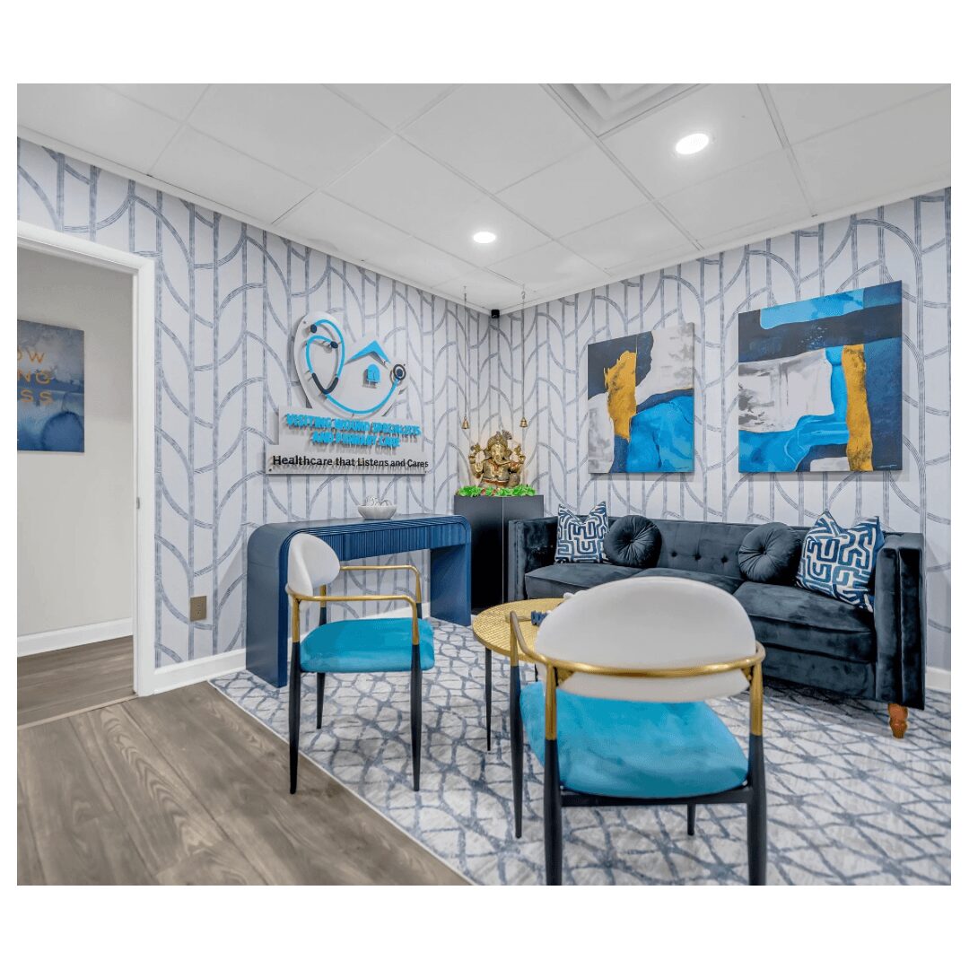 Waiting room with blue and white decor, a black sofa, two chairs, wall art, and a patterned rug.