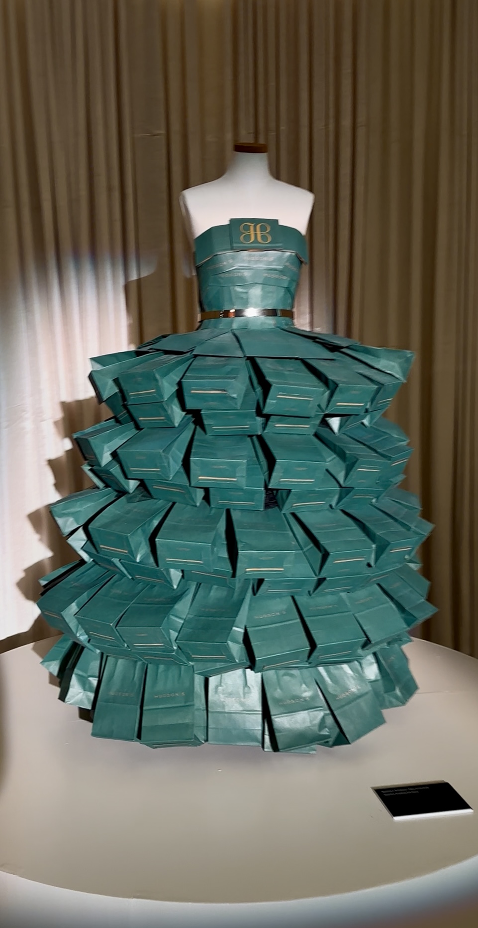 Dress with a fitted bodice and a full, layered skirt made of teal-colored paper or fabric, displayed on a mannequin.