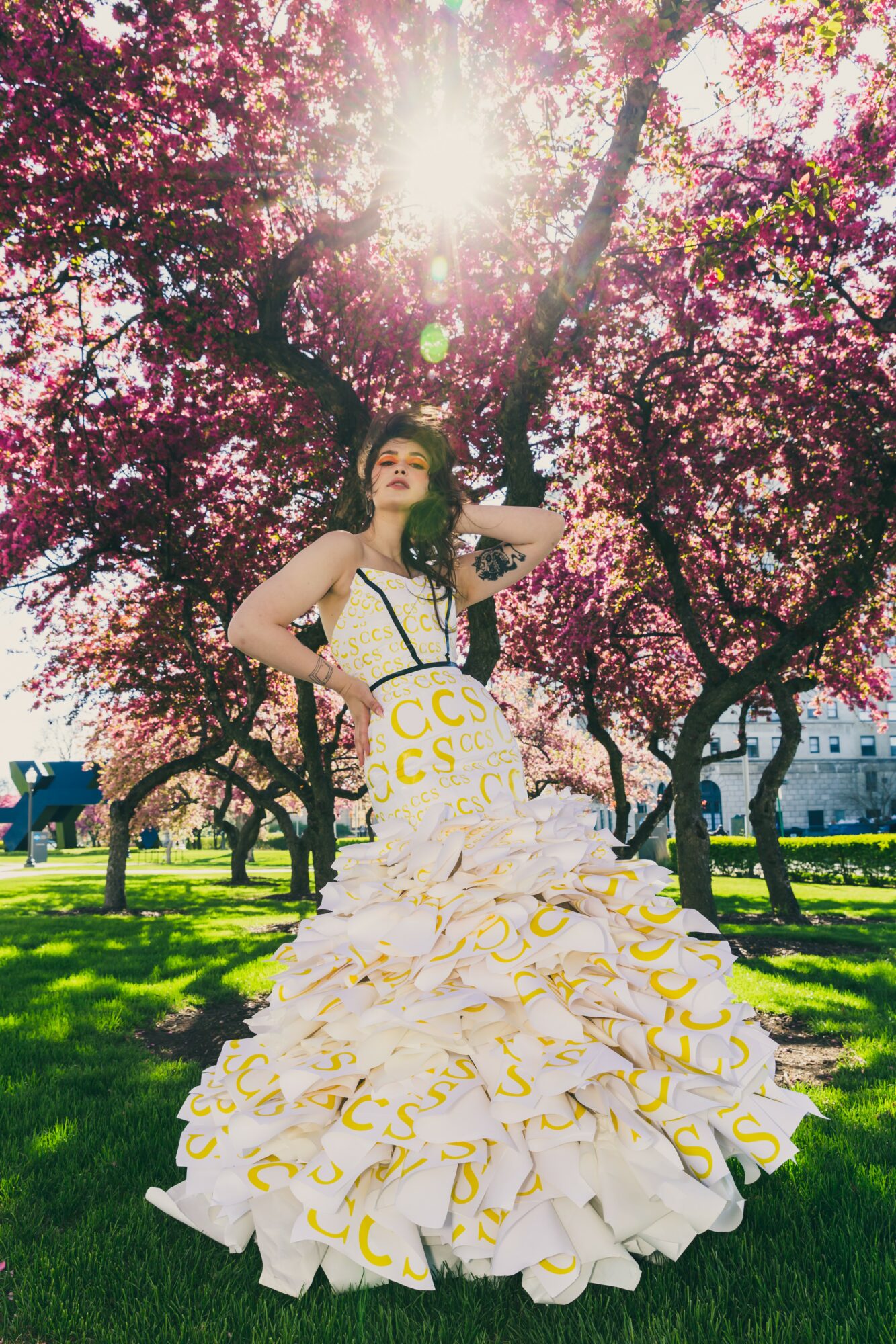 Woman in a white and yellow ruffled dress standing under pink flowering trees with sunlight shining through branches