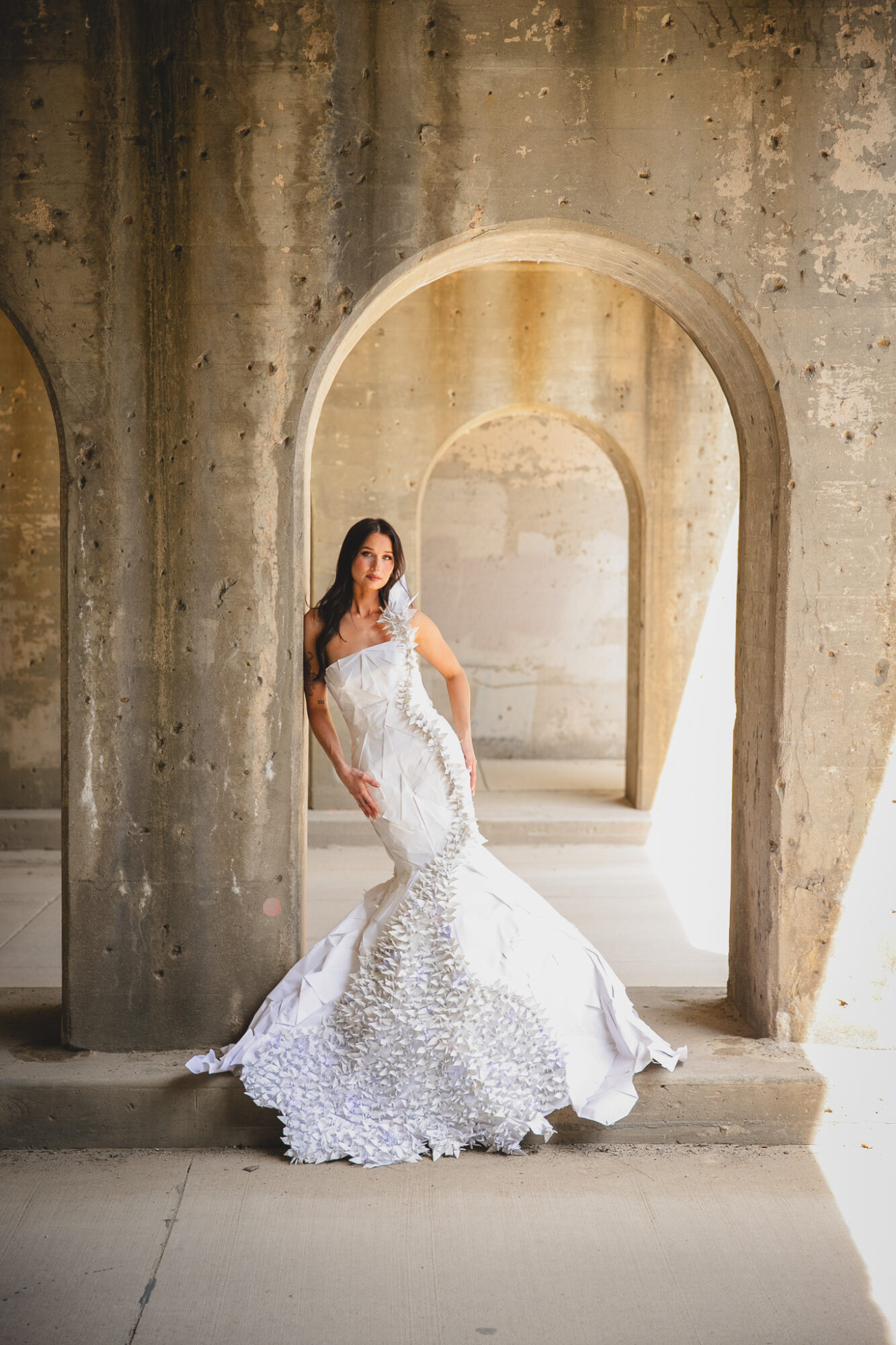 Woman in a white wedding dress standing in an arched stone doorway, with textured stone walls behind her.