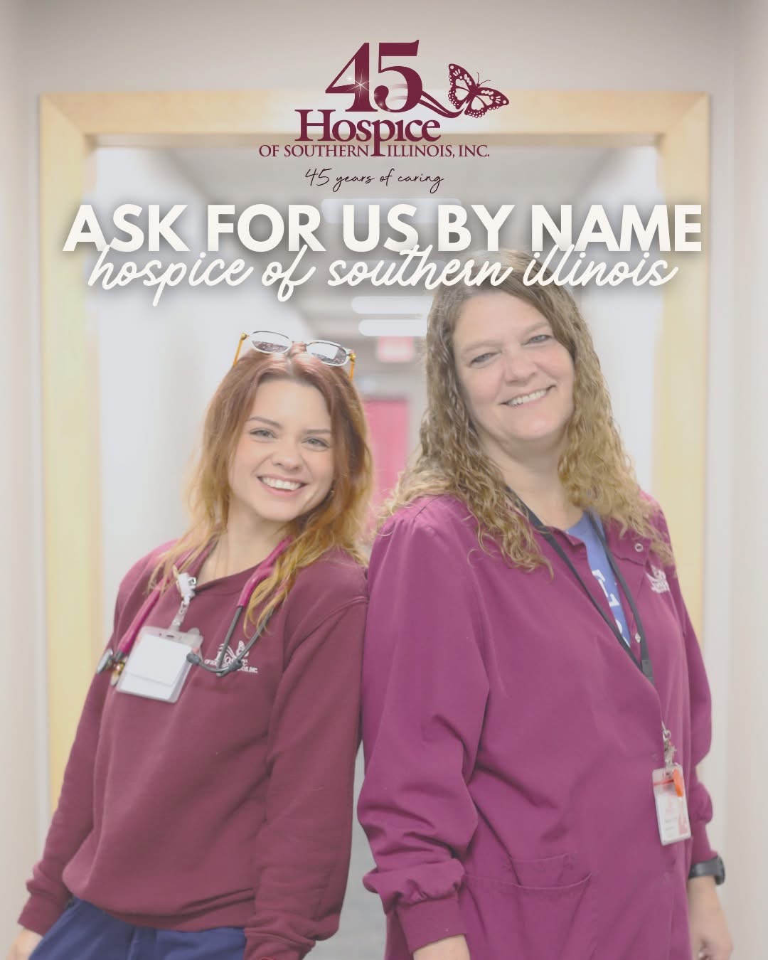 Two smiling women in purple scrubs stand in front of a hospital entrance with a sign for Hospice of Southern Illinois, smiling at the camera.
