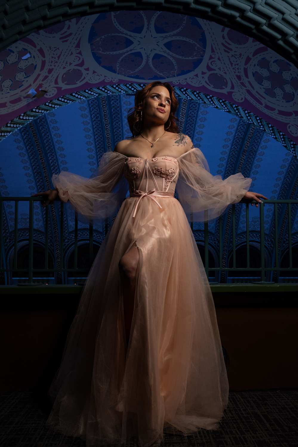 Woman in a flowing gown standing on a balcony with a decorative blue and purple background.