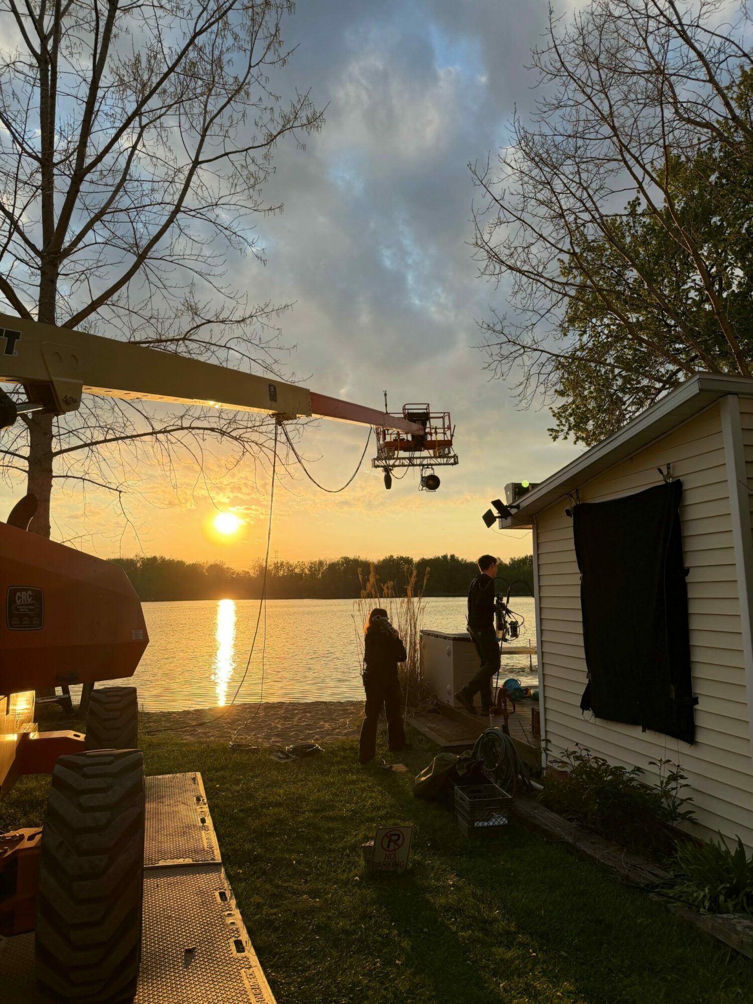 Sunset over a body of water with trees and a person standing outside a small building.