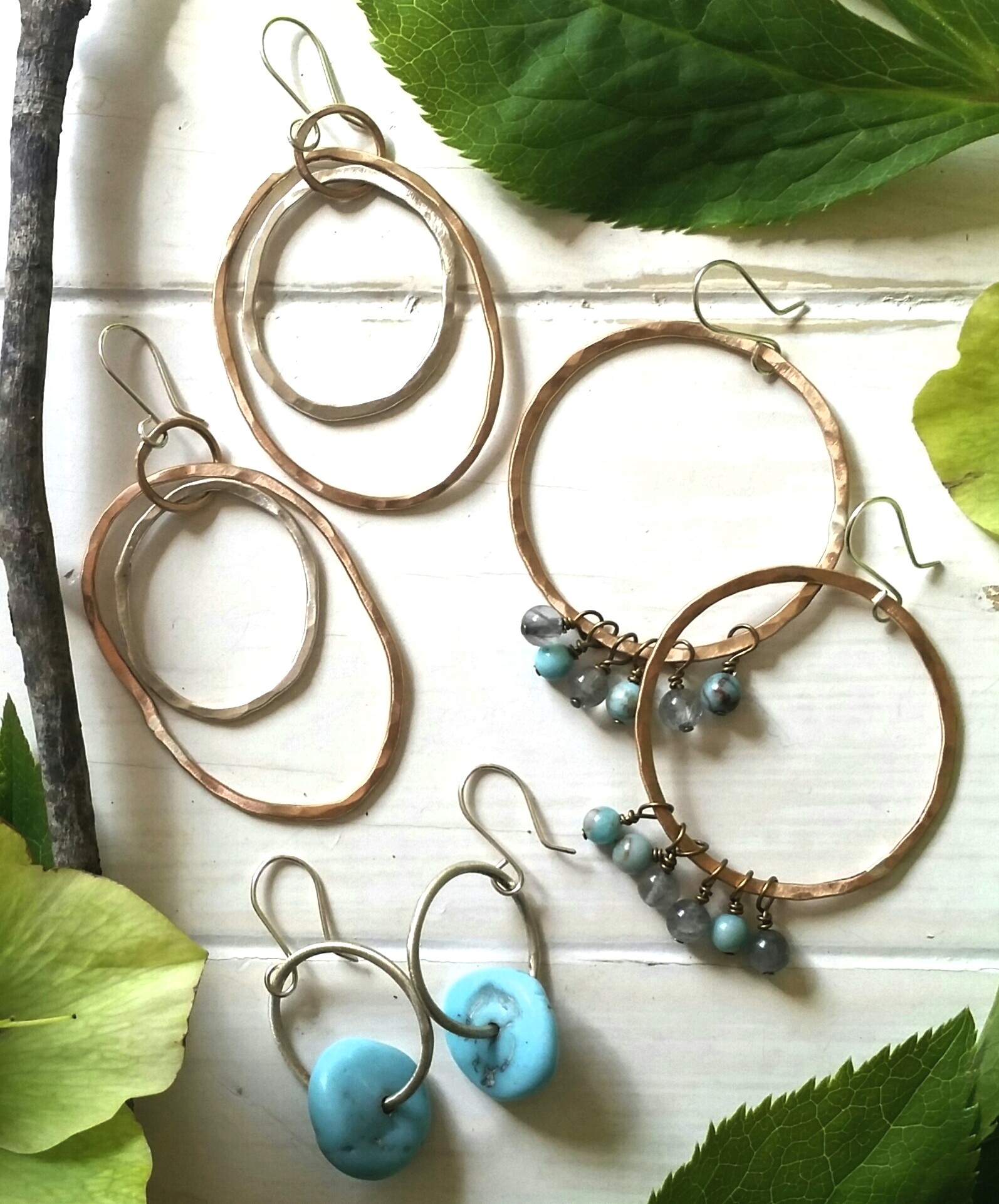 Six pairs of hoop earrings with various sizes and designs, some with beads, arranged on a white surface with green leaves.