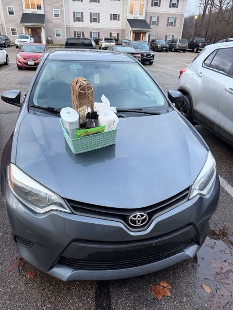 Gray Toyota car parked outdoors with a green basket containing cleaning supplies on the hood.