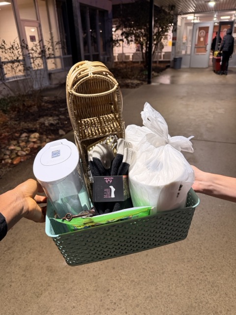 Person holding a green basket with a wicker chair, white plastic bag, black box, and a white container outside at night.