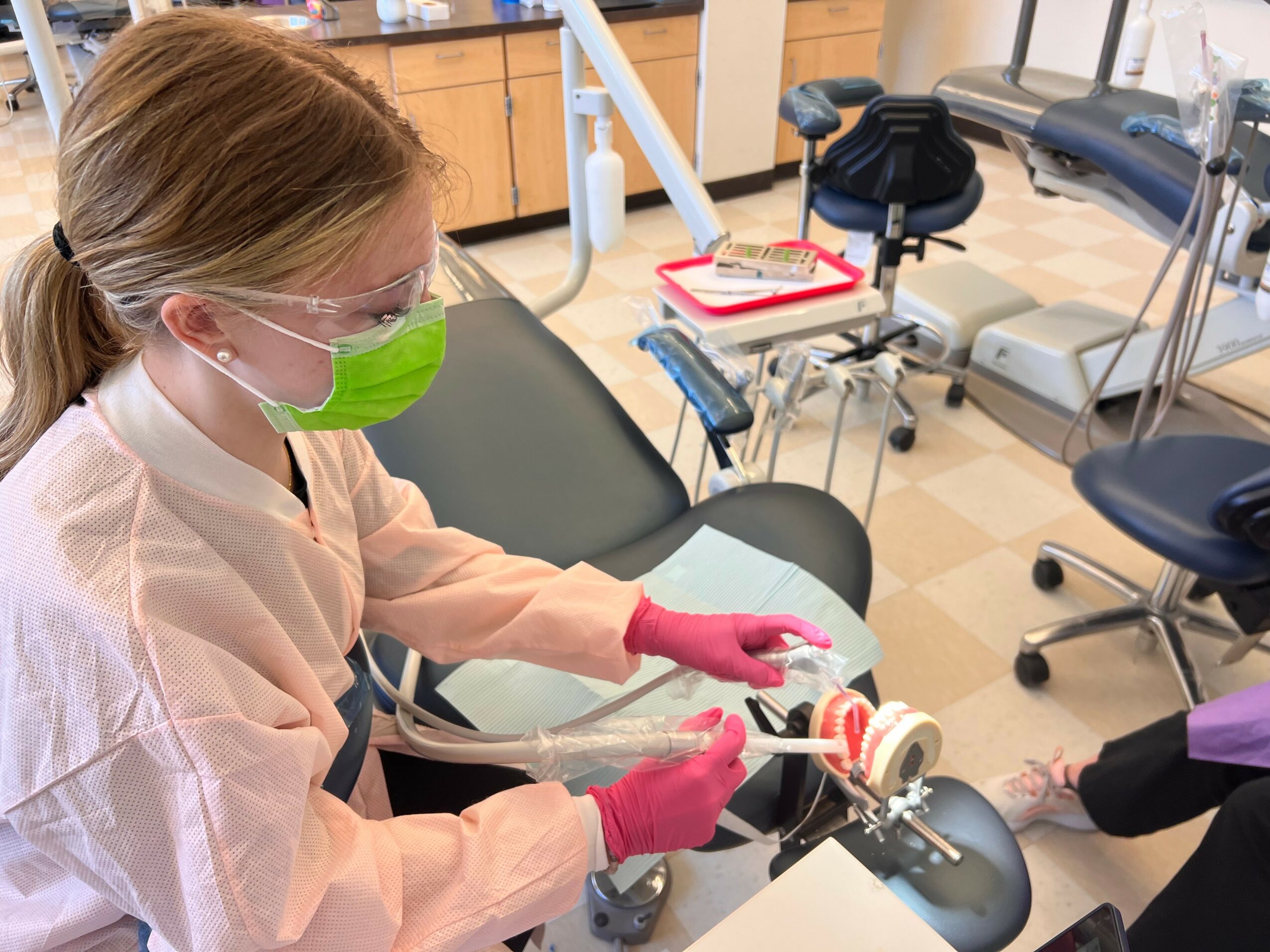 Dental professional wearing protective gear, including a green mask and pink gloves, working on a patient in a dental clinic.