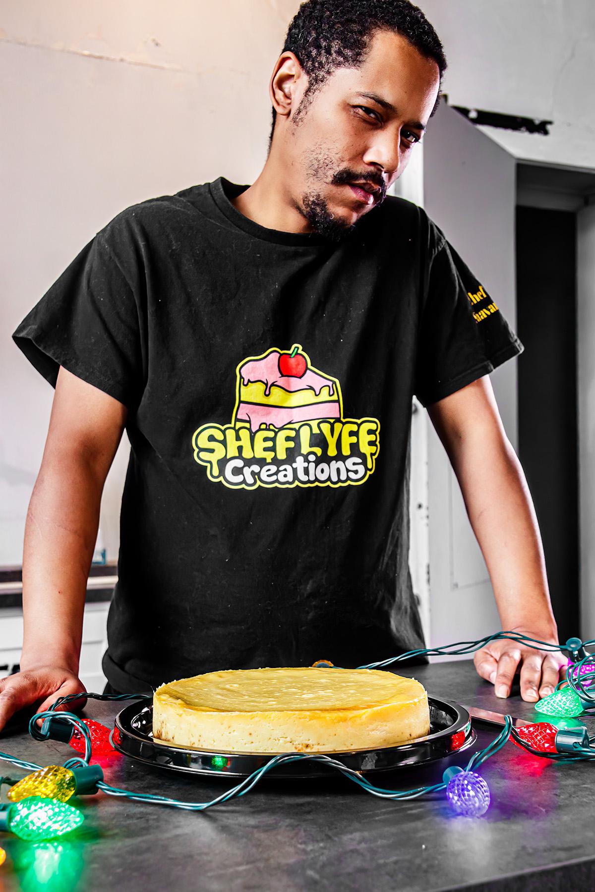 Man with short hair and beard looking down at a cake decorated with colorful lights, wearing a black T-shirt with a logo.